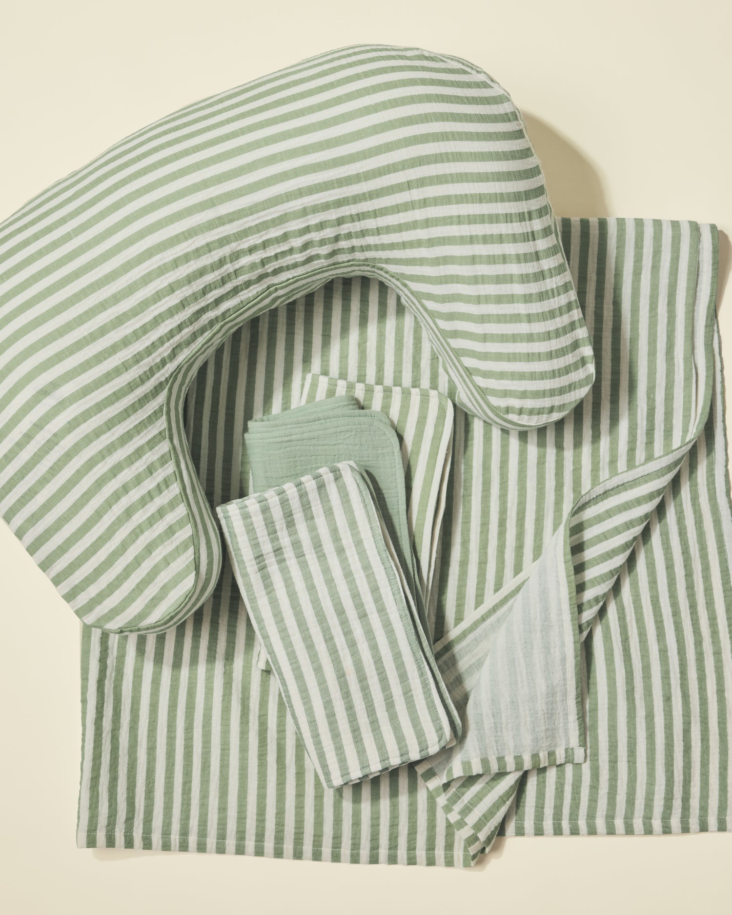 Set of green and white striped nursing pillow, burp cloths and swaddle on a light background