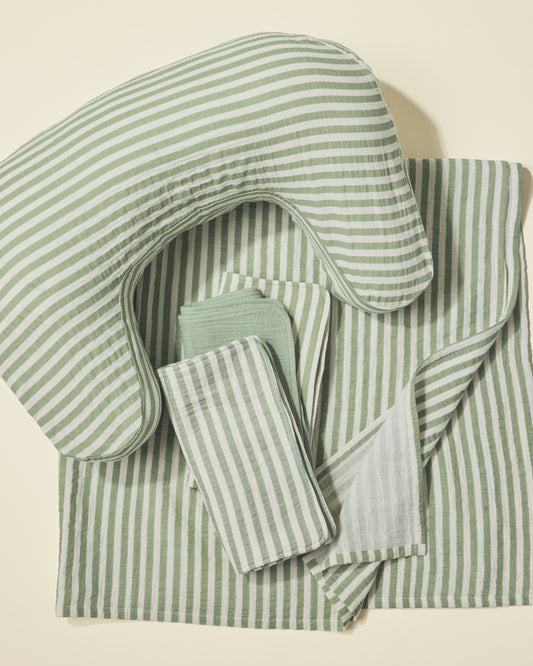 Set of green and white striped nursing pillow, burp cloths and swaddle on a light background