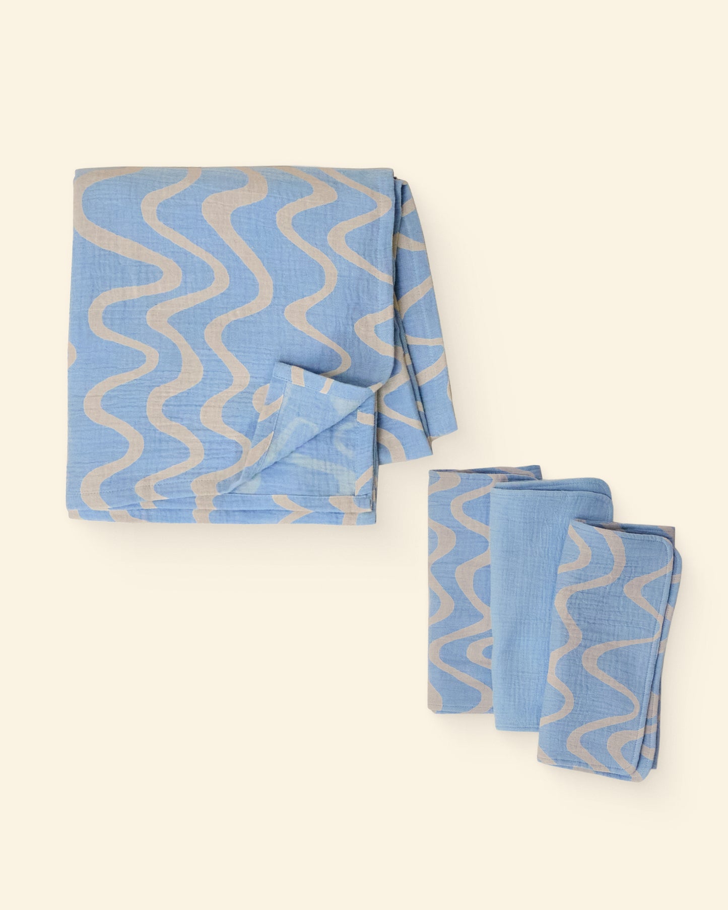 Set of blue and white wave patterned burp cloths and swaddle on a light background
