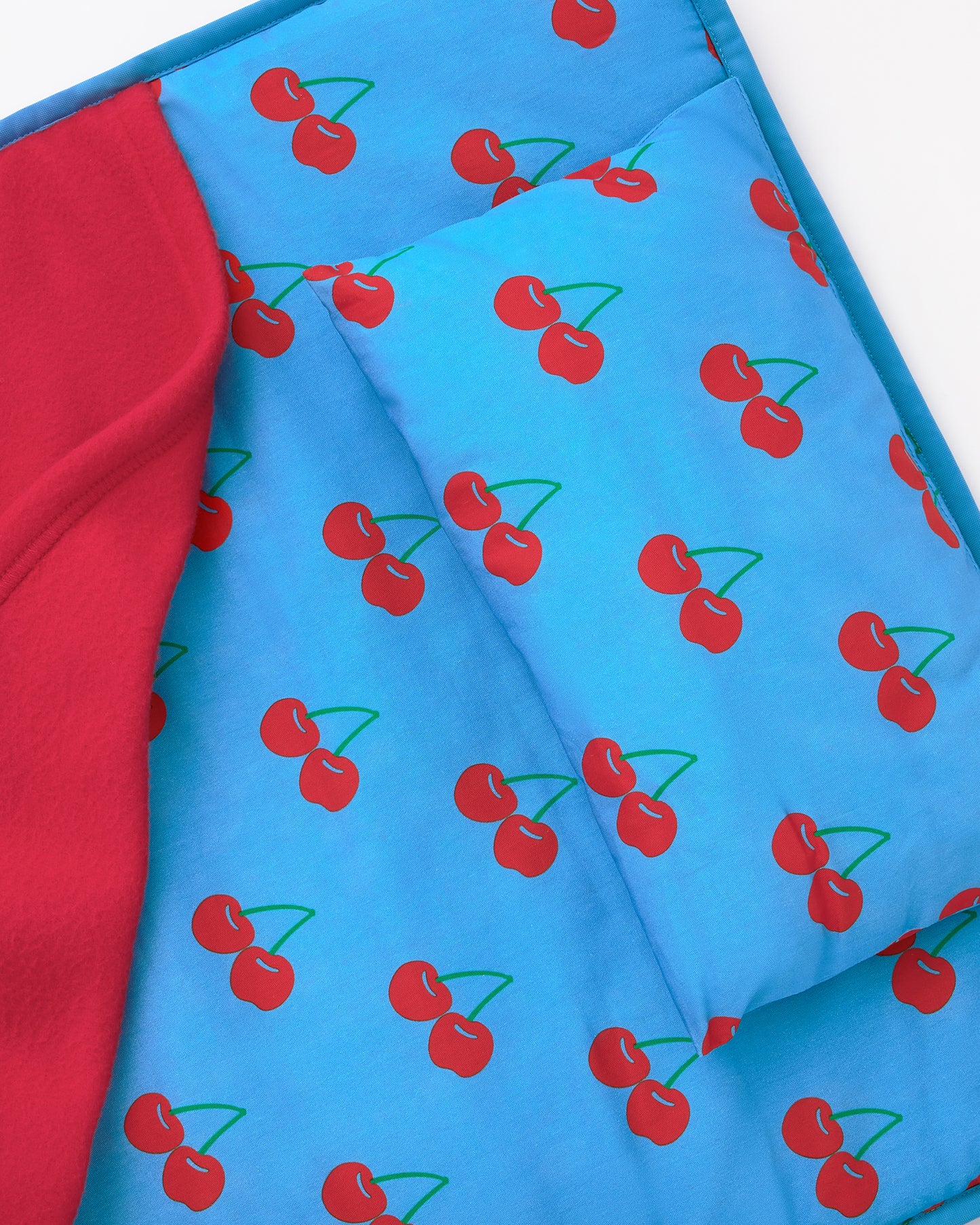 Close up of the pillow on the Nap Mat in Blue Cherries pattern on a beige background.