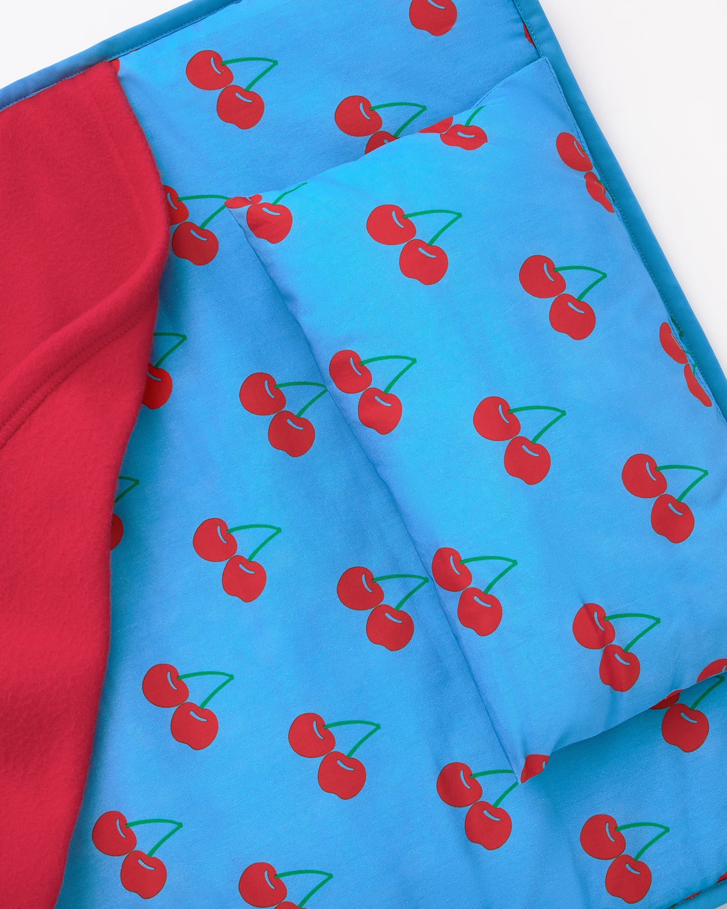 Close up of the pillow on the Nap Mat in Blue Cherries pattern on a beige background.