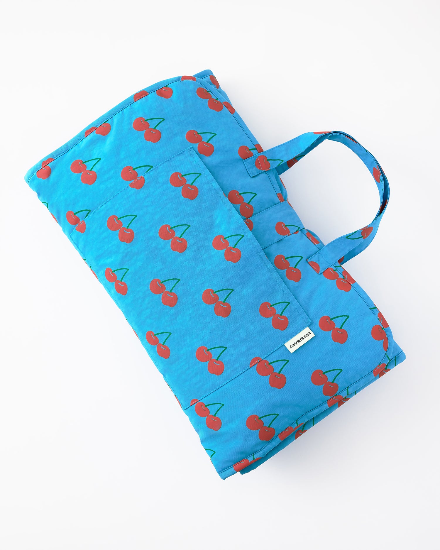 Close up of the folded up view of the Nap Mat in Blue Cherries pattern on a beige background.