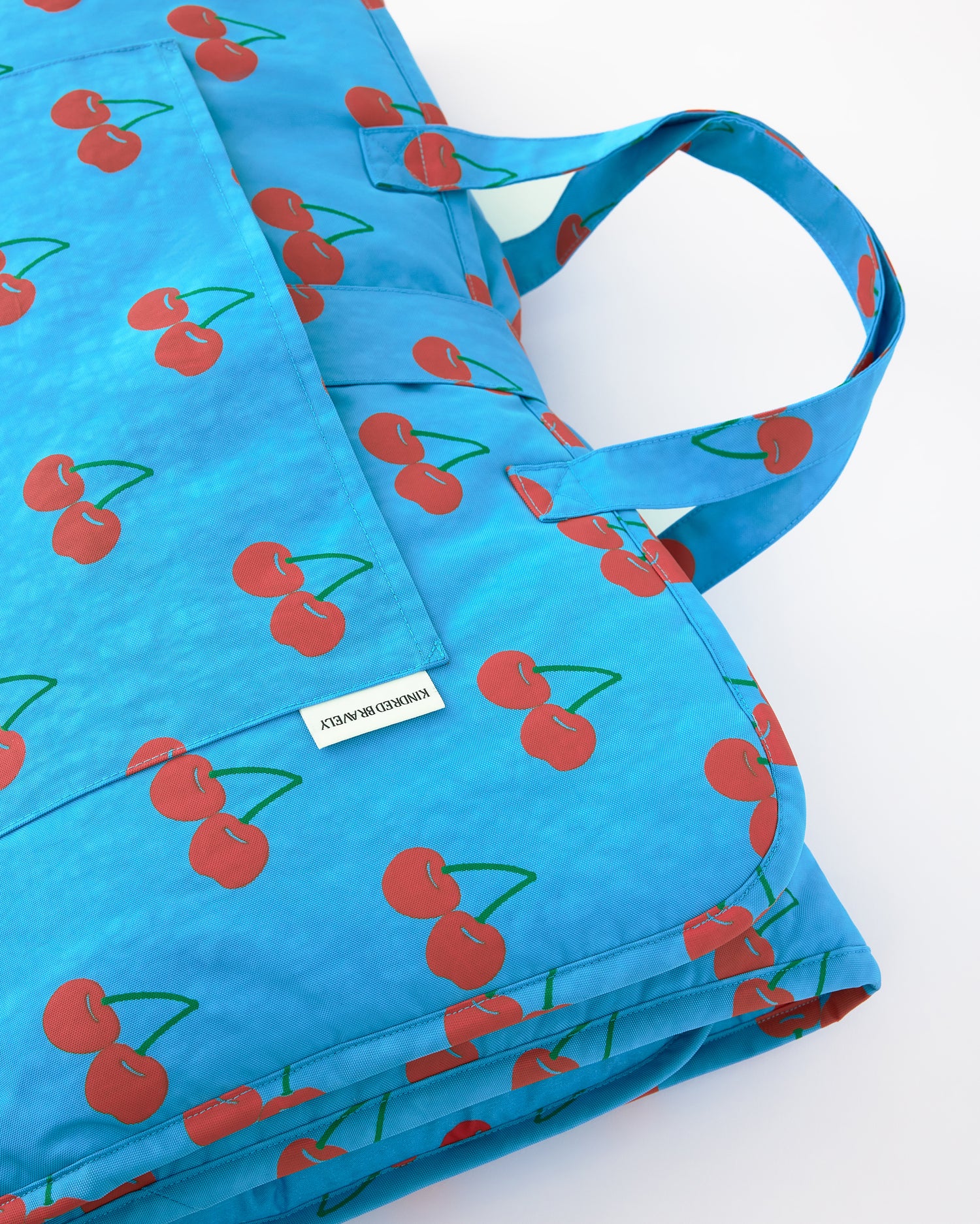 Close up of the folded up view of the Nap Mat in Blue Cherries pattern on a beige background.