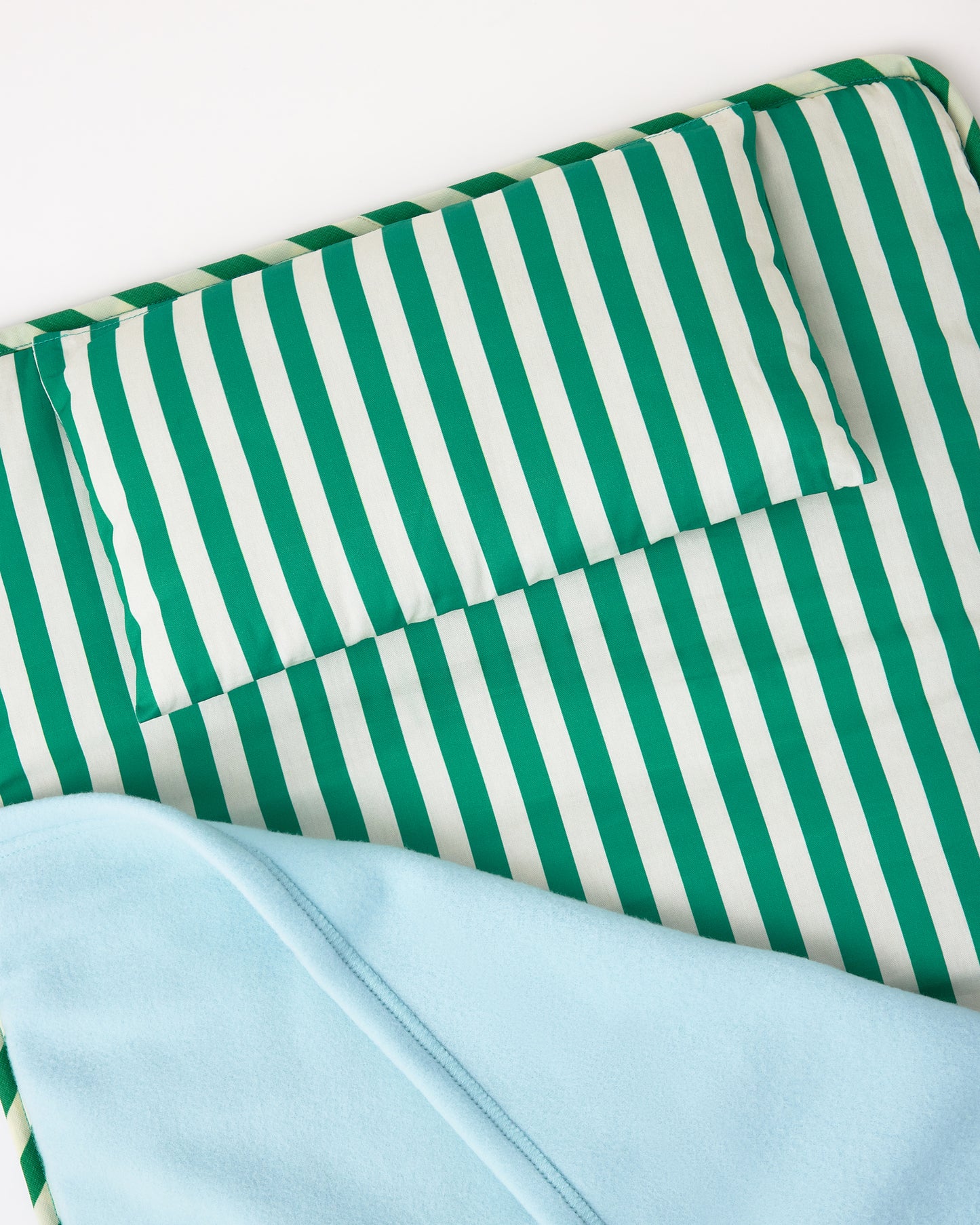 Close up of Nap Mat in Green Stripe with lightly padded mat, pillow and light blue Soft fleece blanket that can fold over, velcro closure, handle for carrying, on a white background.