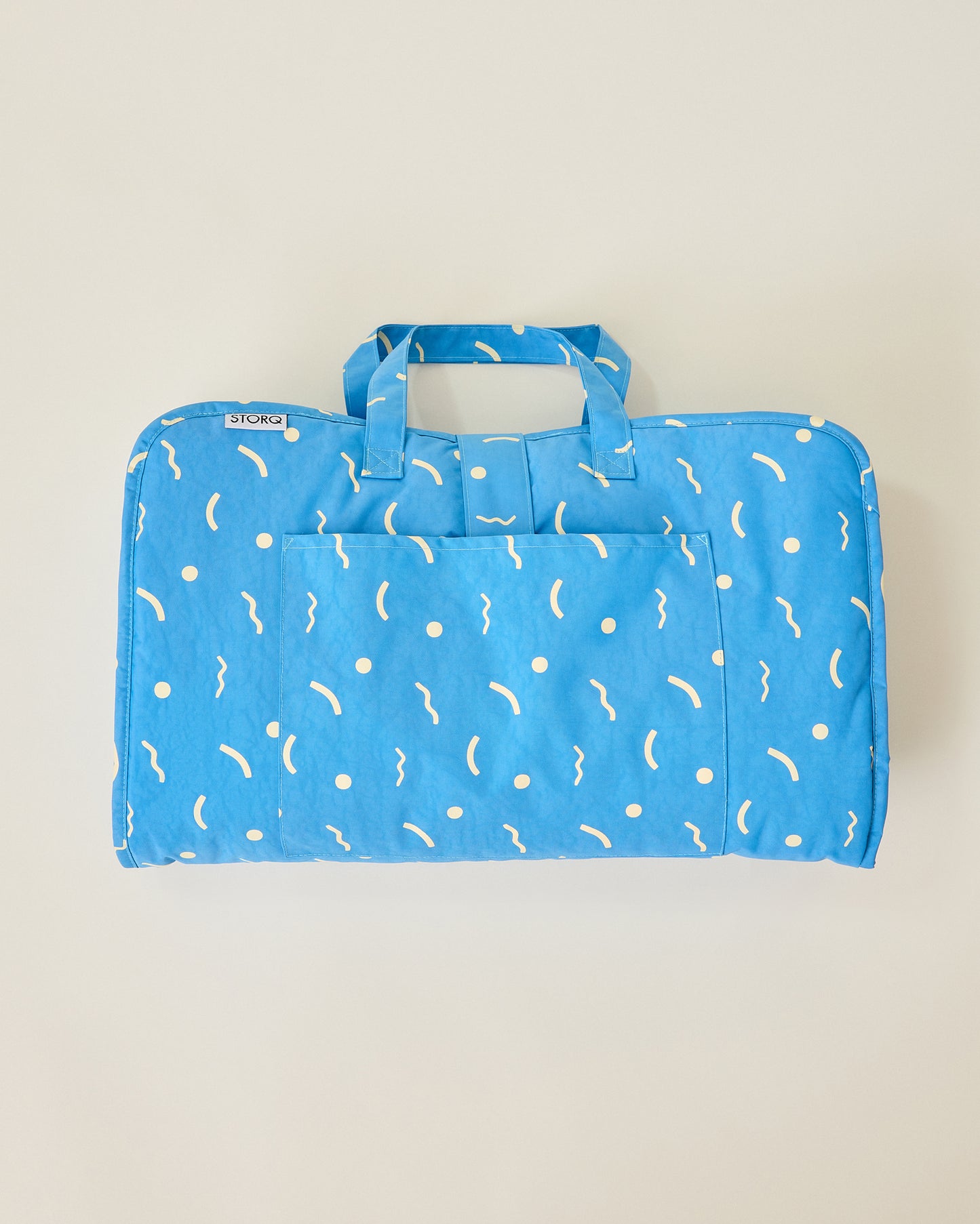Folded up Nap Mat in solid blue and sky squiggles pattern with handles on beige background