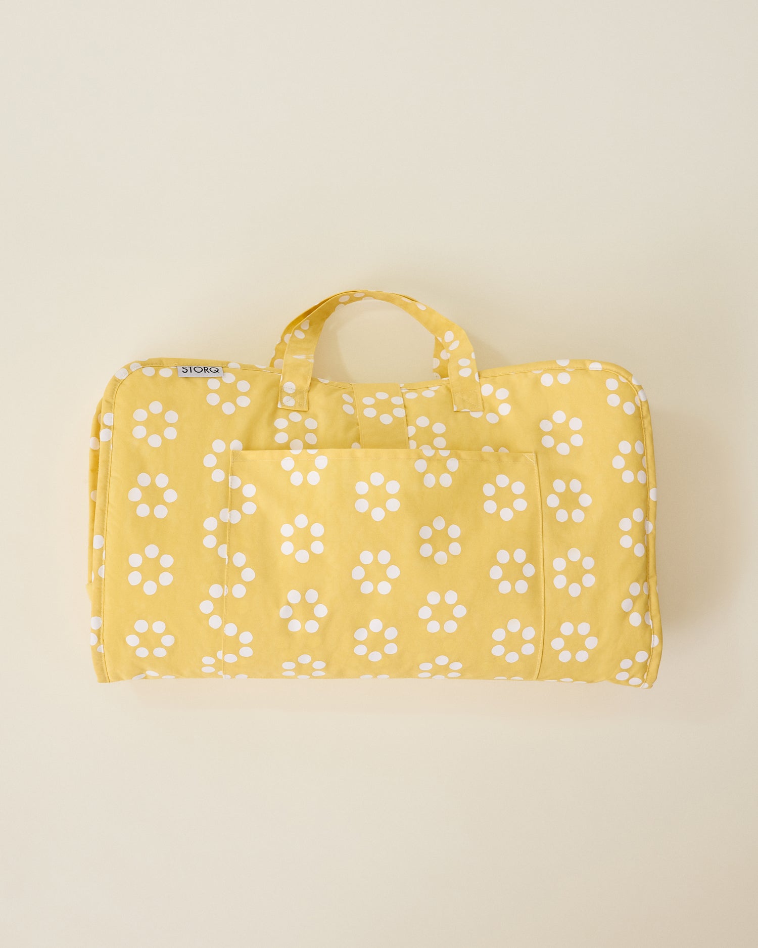 Folded up Nap Mat in yellow sunshine dots pattern with handle on beige background