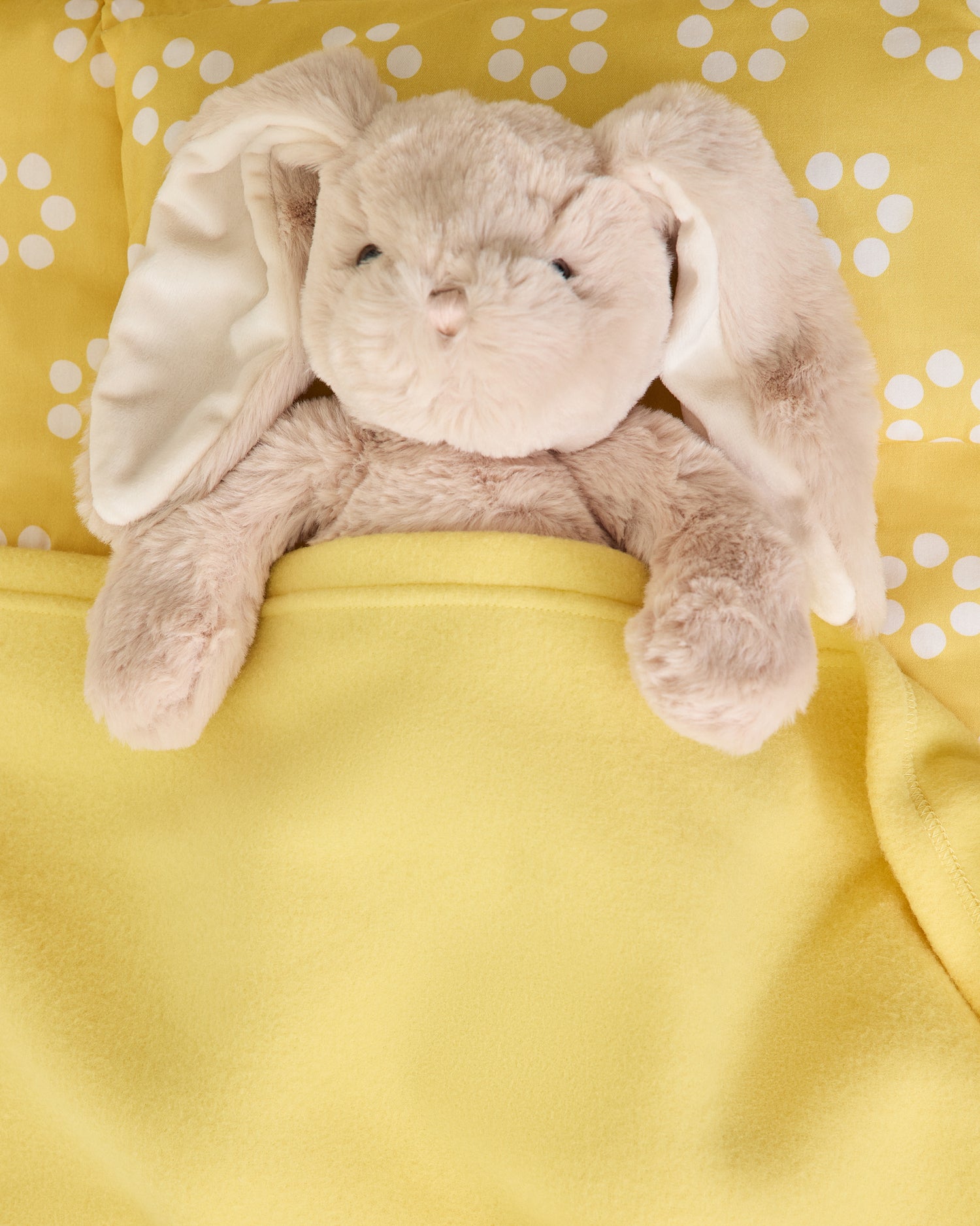 Plush bunny tucked in to Nap Mat in yellow sunshine dots pattern
