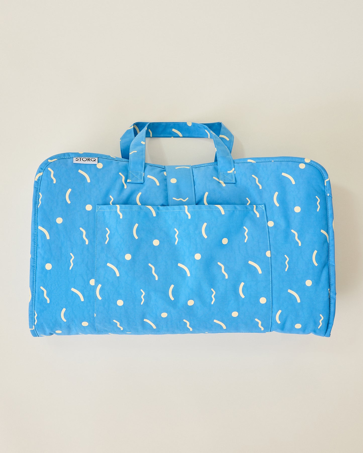 Folded up Nap Mat in solid blue and sky squiggles pattern with handles on beige background