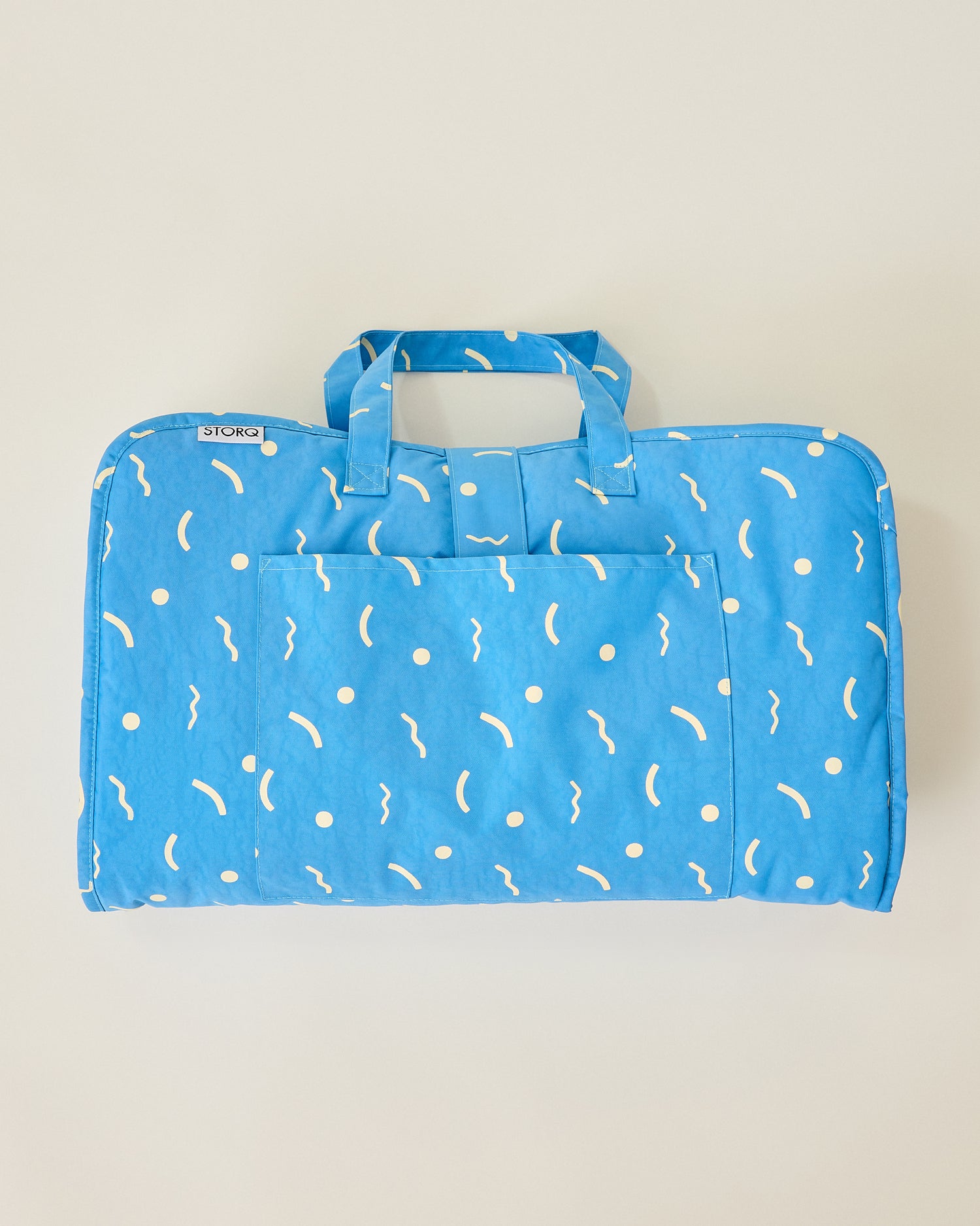 Folded up Nap Mat in solid blue and sky squiggles pattern with handles on beige background