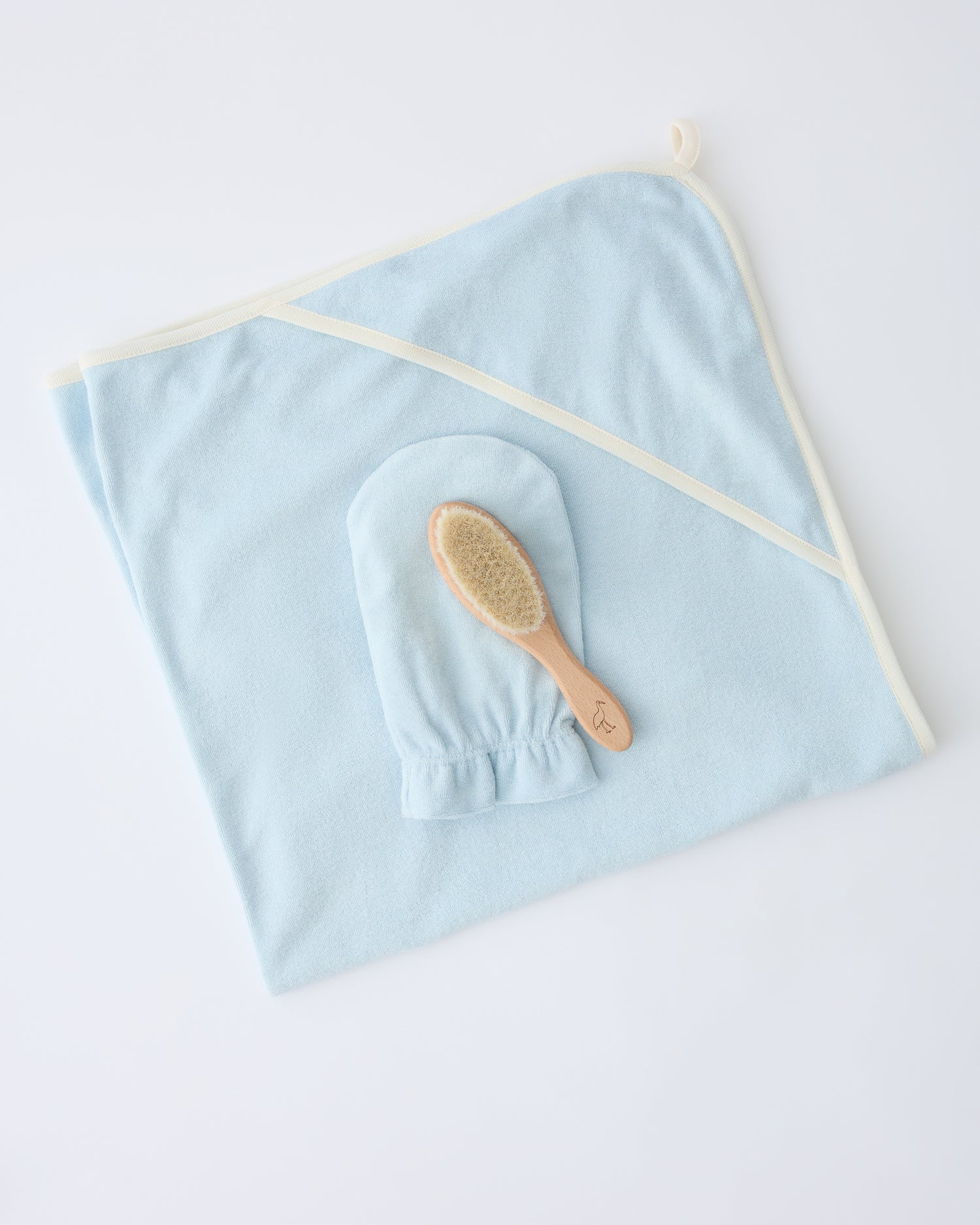 Newborn Bath Set in Breeze, including hooded towel, hair brush and bath mitt, on a beige background.