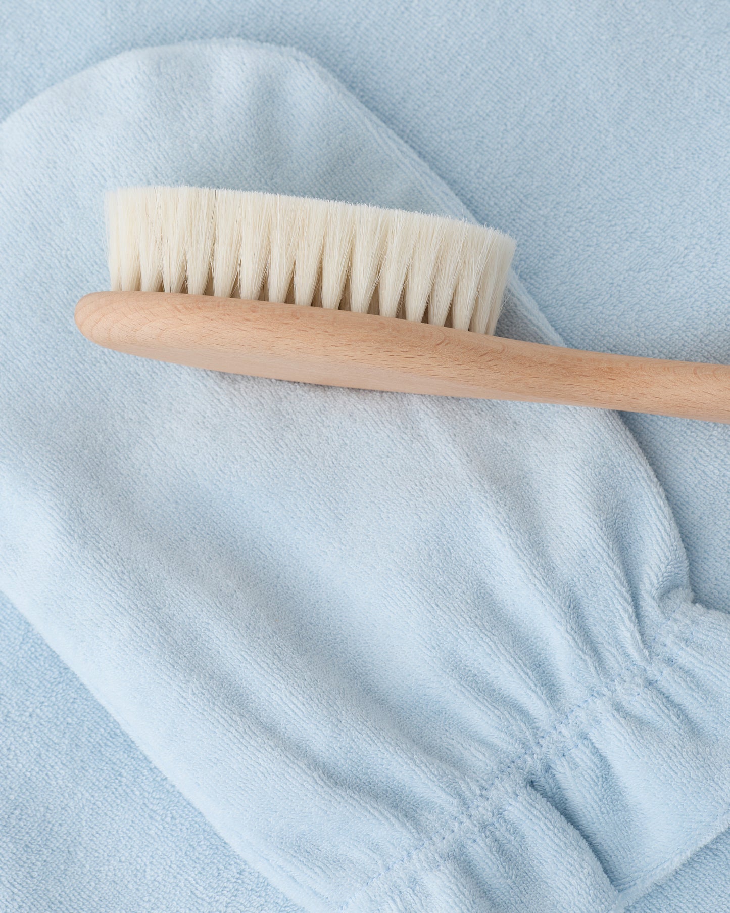 Newborn Bath Set in Breeze, including hooded towel, hair brush and bath mitt, on a beige background.