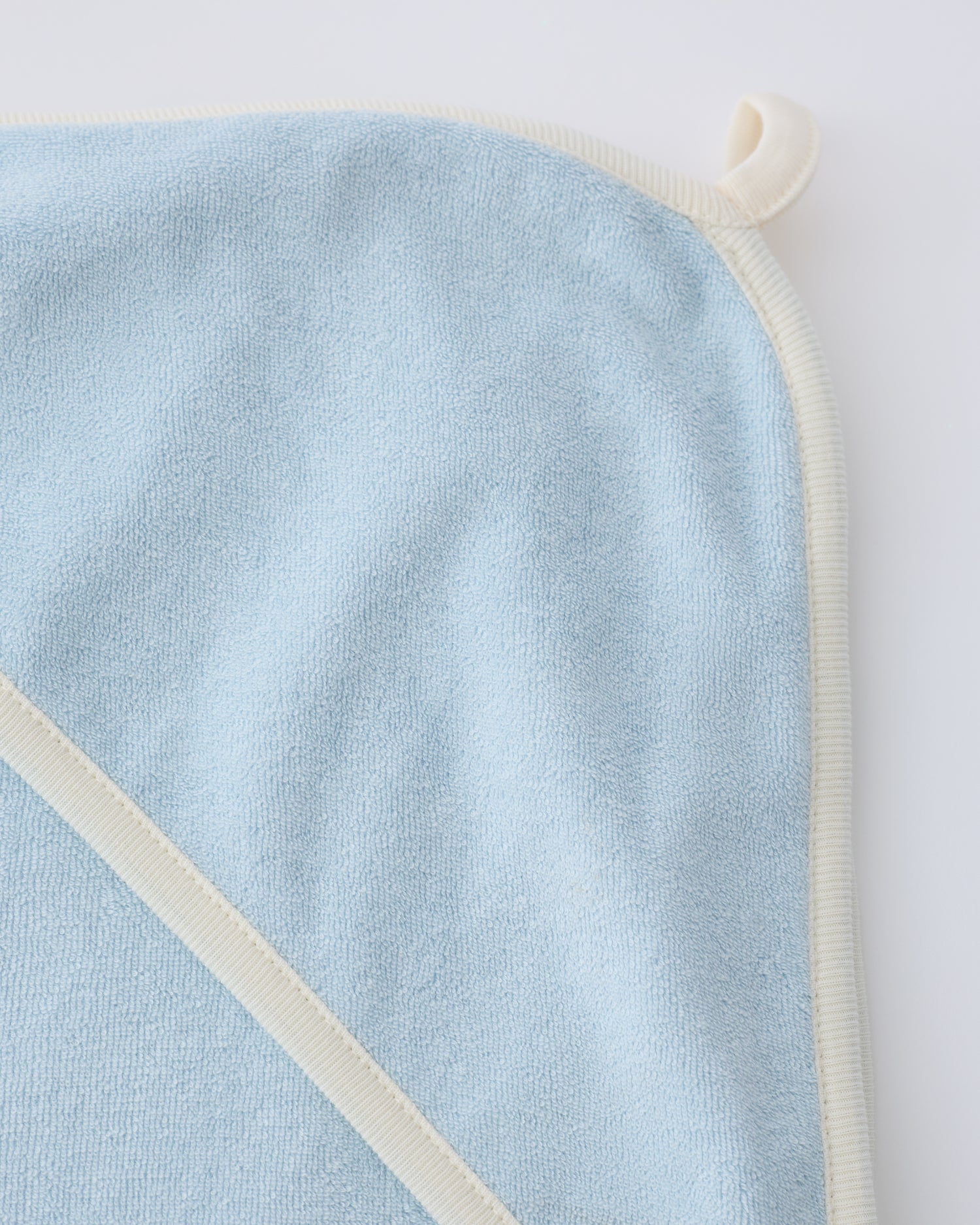 Close up of the hanging loop on the hooded towel in the Newborn Bath Set in Breeze, on a beige background.