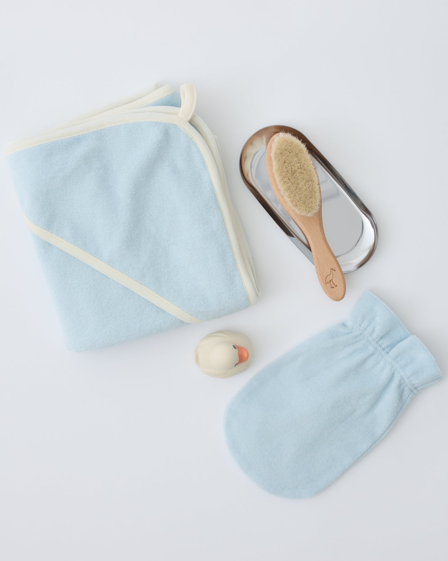 Newborn Bath Set in Breeze, including hooded towel, hair brush and bath mitt with brush on metallic soap dish next to rubber ducky, on a beige background.