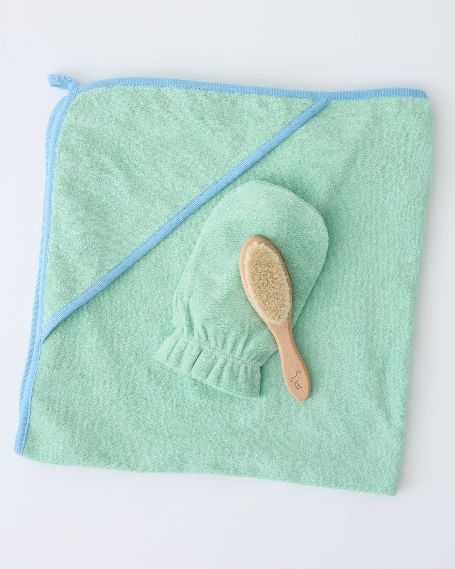 Newborn Bath Set in Mint, including hooded towel, hair brush and bath mitt, on a beige background.