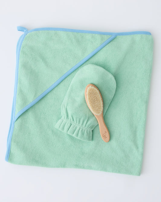 Newborn Bath Set in Mint, including hooded towel, hair brush and bath mitt, on a beige background.