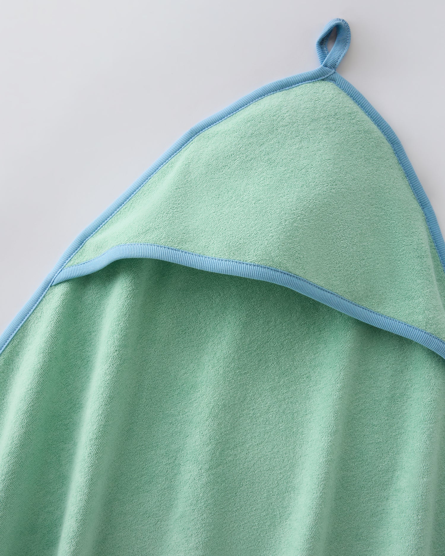Close up of the hooded towel hanging loop in the Newborn Bath Set in Mint, on a beige background.