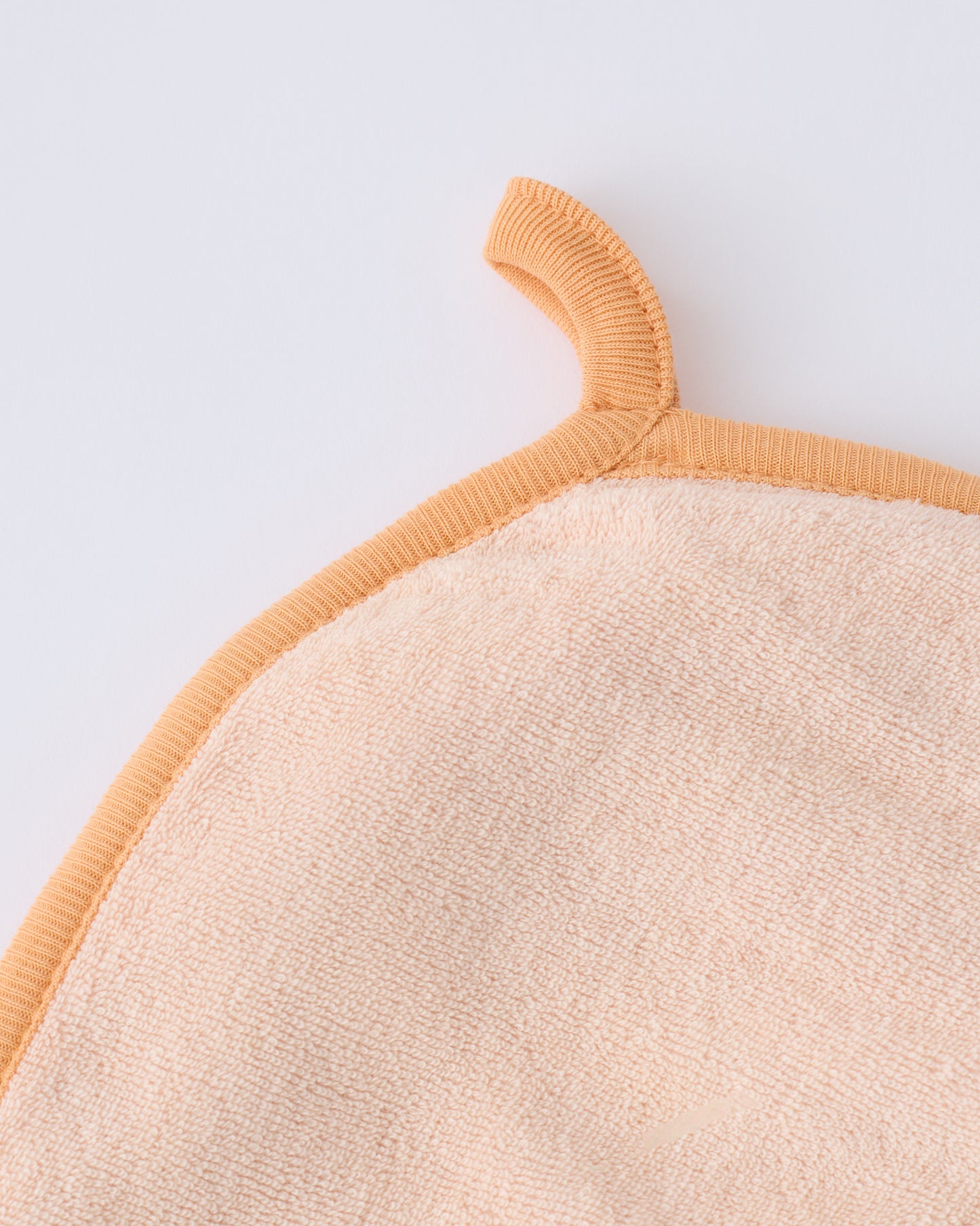 Close up of the hanging loop on the hood of the towel within the Newborn Bath Set in Peach Whip, on a beige background.