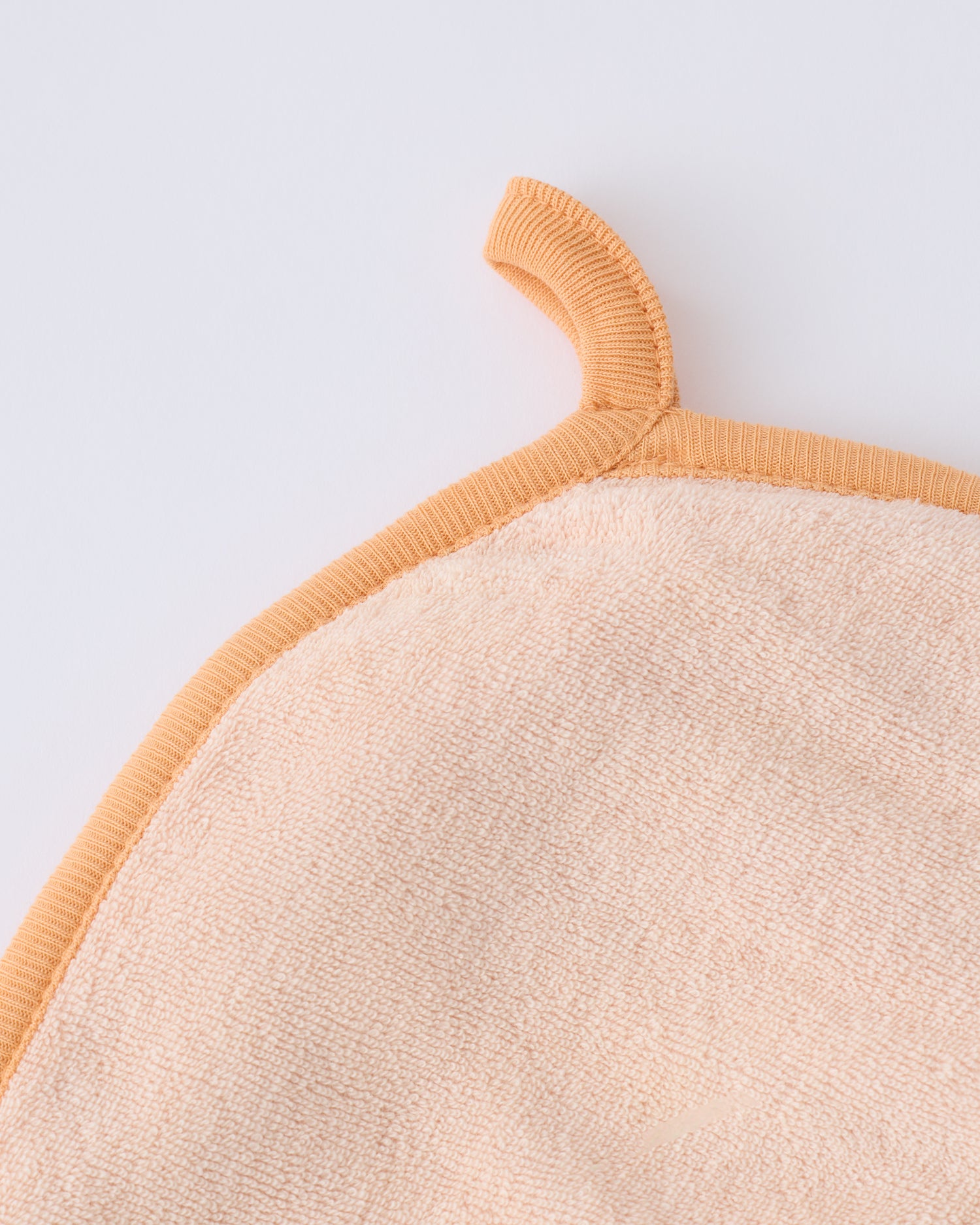 Close up of the hanging loop on the hood of the towel within the Newborn Bath Set in Peach Whip, on a beige background.