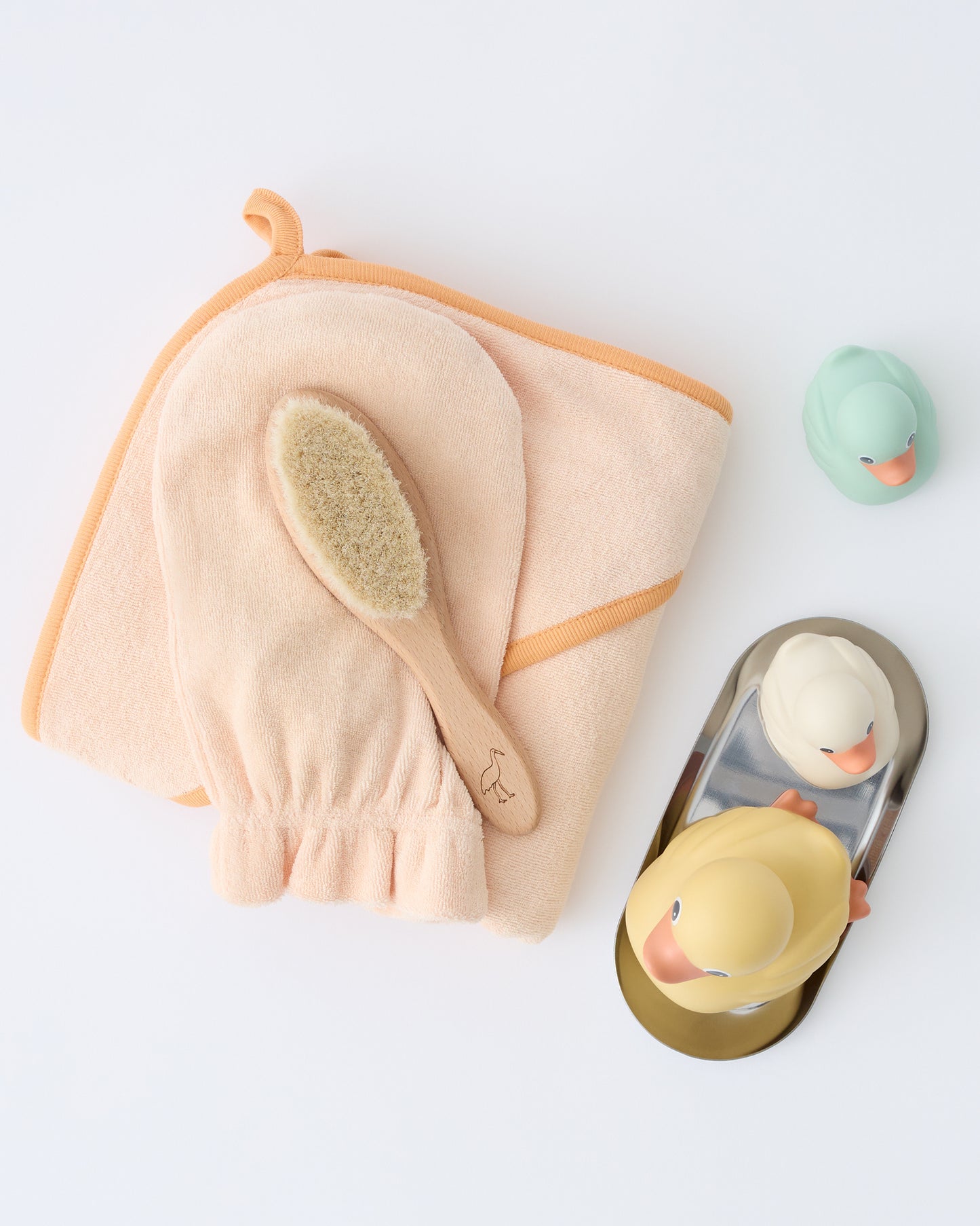 Newborn Bath Set in Peach Whip, including hooded towel, hair brush and bath mitt and decorated with metallic soap dish and three rubber duckies on a beige background.