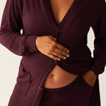 Pregnant model wearing a deep burgundy cardigan over matching pants on a neutral background