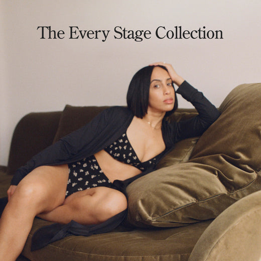 Black text states: The Every Stage Collection. Image of model resting on sofa wearing Every Stage Triangle Bralette, Every Stage Brief in Black Wildflower and The Sunday Lounge Duster in Black. Light filled walls  in background.