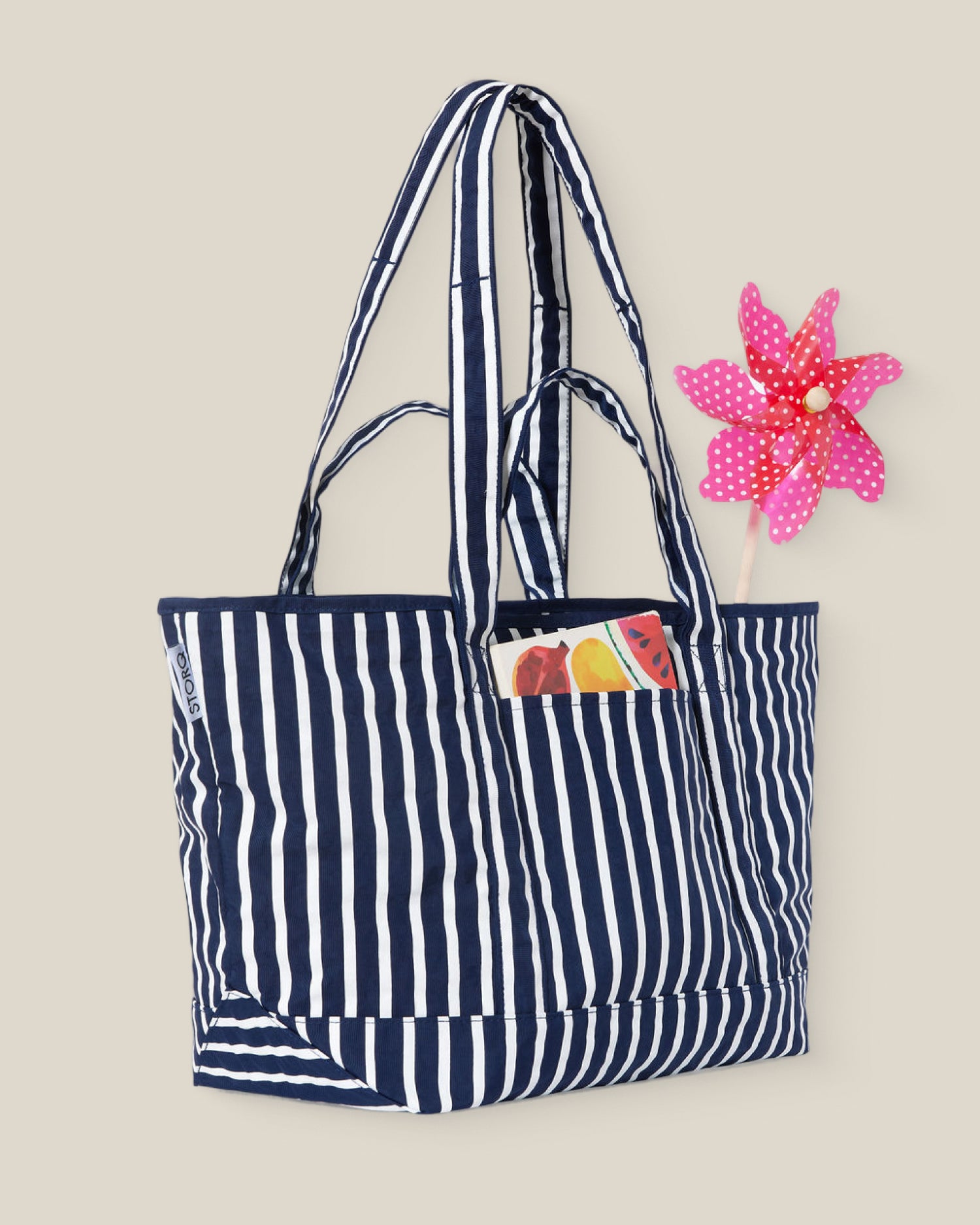 Navy blue and white striped Packable Park Carryall with items sticking out on a beige background