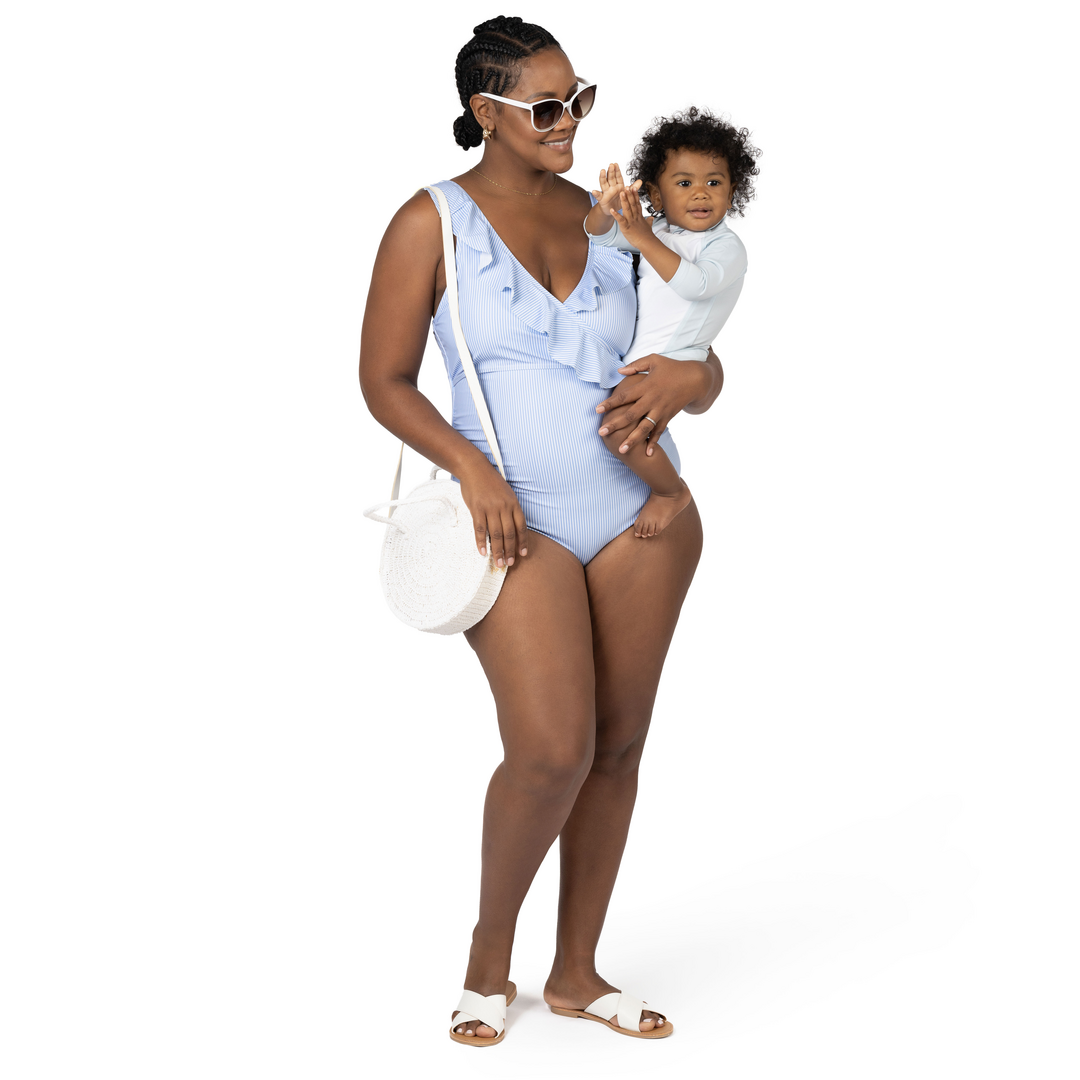 Model carrying her baby while wearing the Ruffle Wrap Maternity & Nursing One Piece Swimsuit in Coastal Stripe