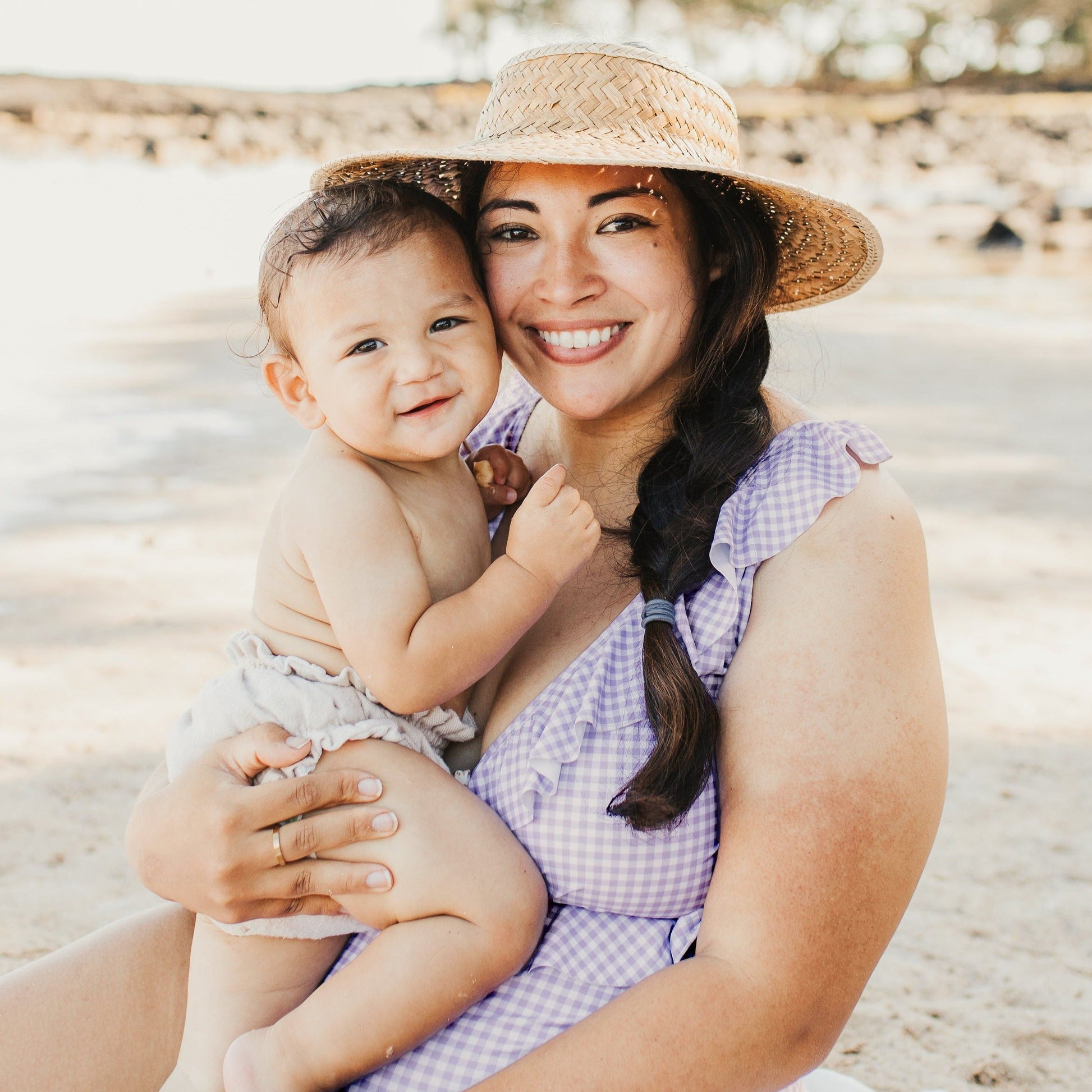 Model smiling with her baby while wearing the Ruffle Wrap Maternity & Nursing One Piece Swimsuit in Lavender Gingham @model_info:Gabby is wearing a Large Busty.