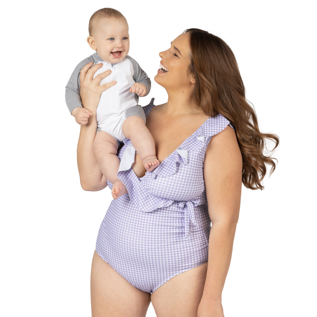 Model holding her baby on her shoulder wearing the Ruffle Wrap Maternity & Nursing One Piece Swimsuit in Lavender Gingham