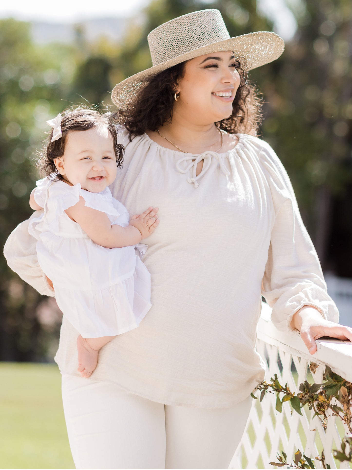 Model wearing the Long Sleeve Nursing Blouse holding her baby on her hip and wearing a hat. @model_info:Lanae is wearing an X-Large.