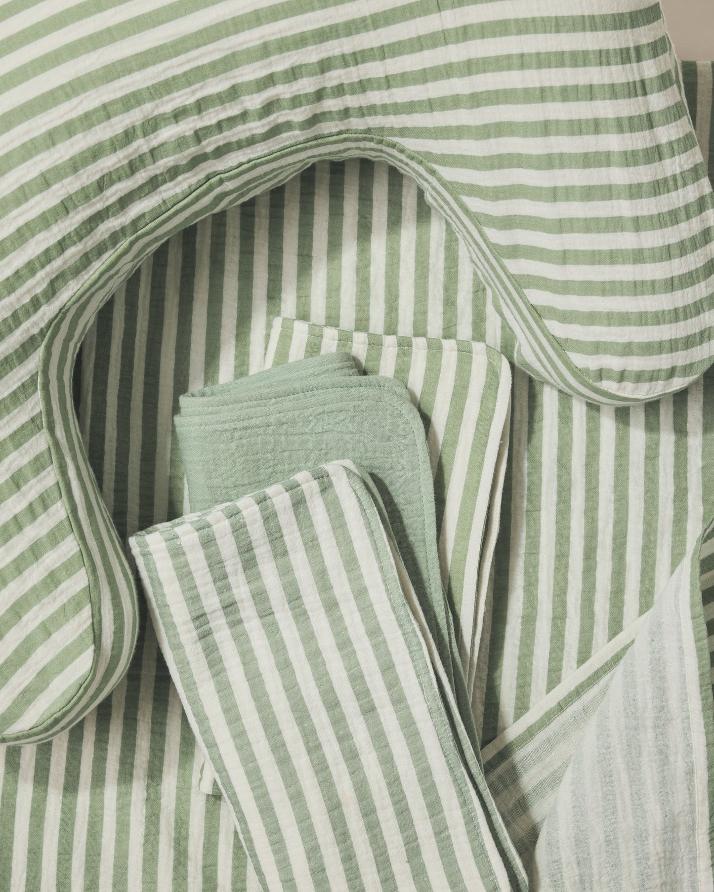 Set of green and white striped nursing pillow, burp cloths and swaddle on a light background