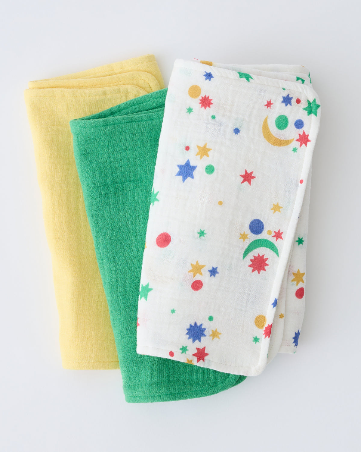 Close up of the Organic Muslin Burp Cloth (Three-Pack) in White Starry Sky pattern, folded and stacked, on a beige background.