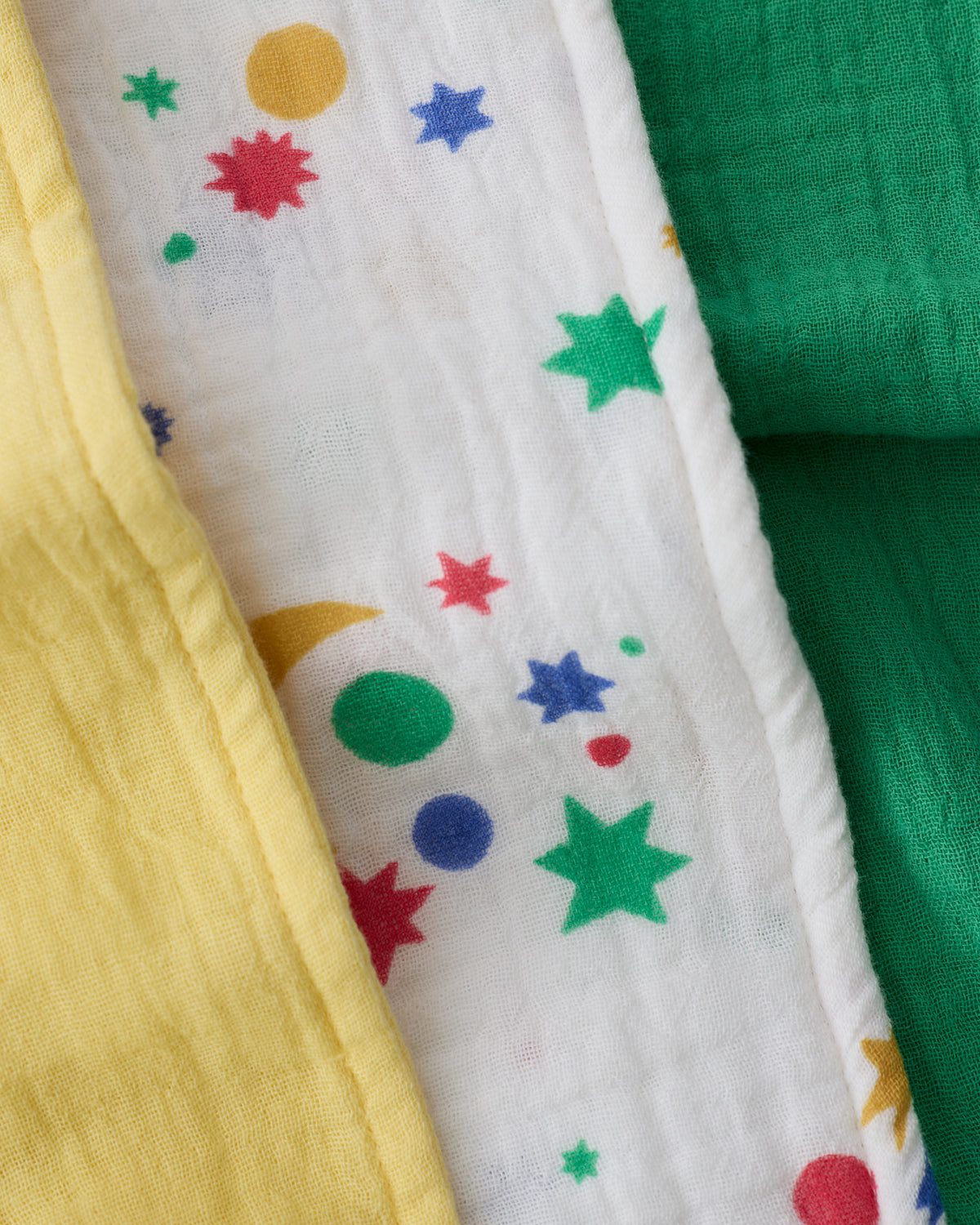Close up of the Organic Muslin Burp Cloth (Three-Pack) in White Starry Sky pattern, folded and stacked, in yellow, stars and green.