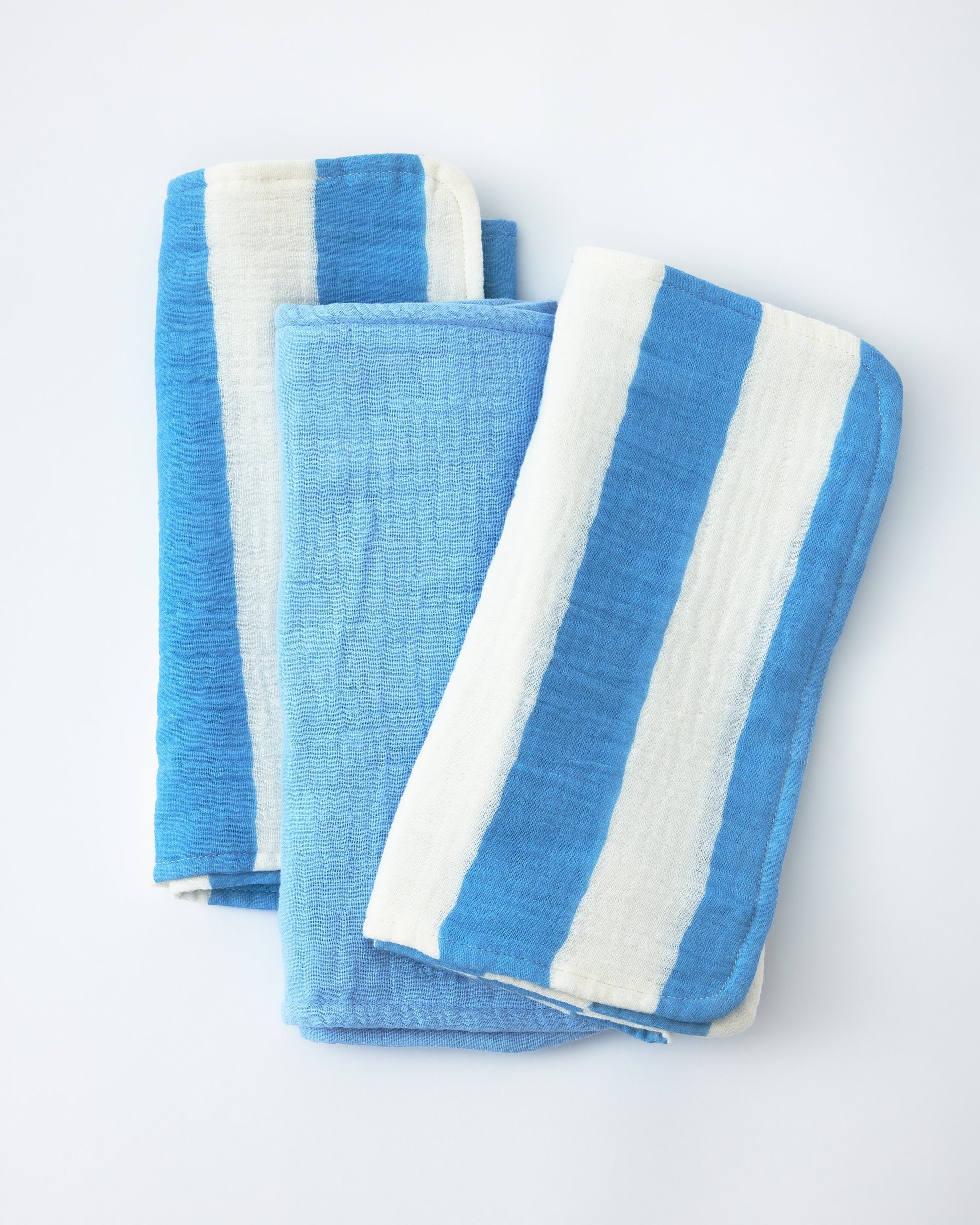 Organic Muslin Burp Cloth (Three-Pack) in Blue Wide Stripe on a beige background.