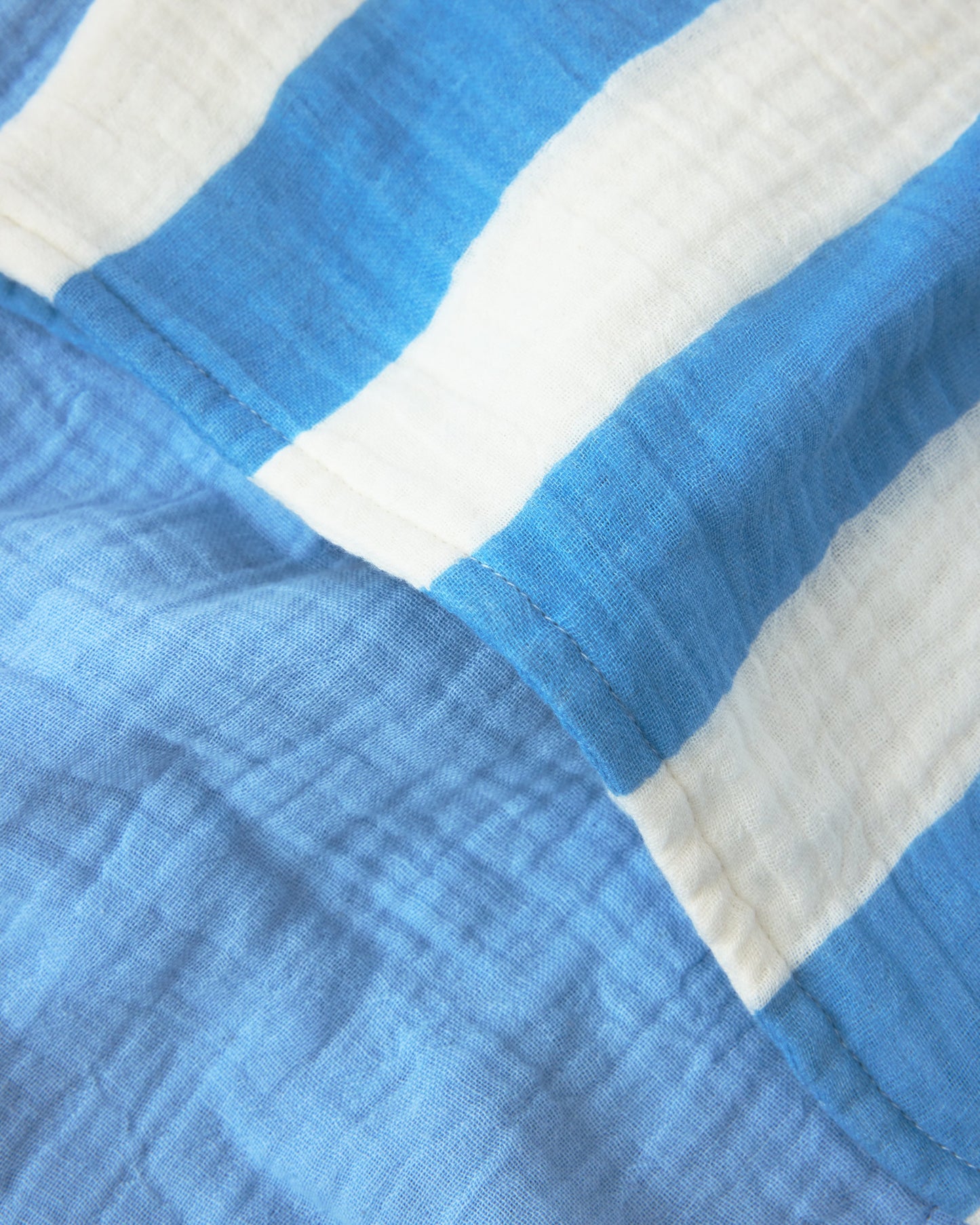 Close up of the Organic Muslin Burp Cloth (Three-Pack) in Blue Wide Stripe to show one side of stripes and the other side of solid blue.