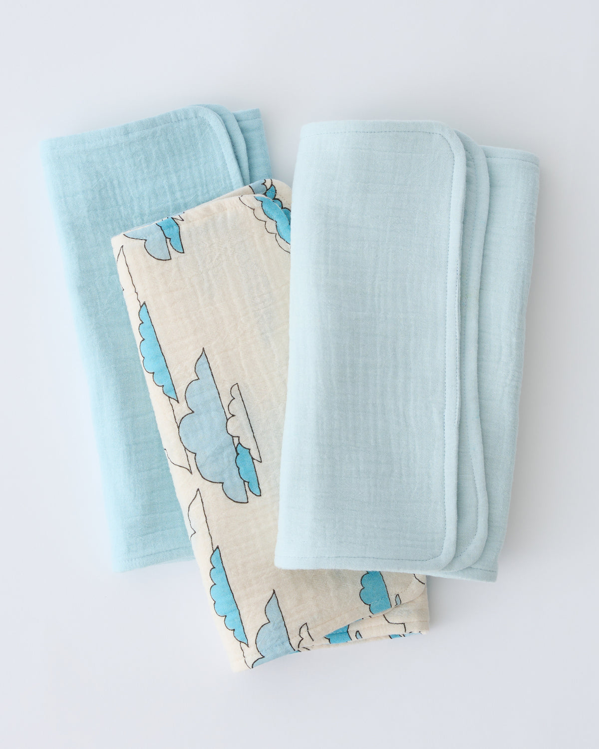 Organic Muslin Burp Cloth (Three-Pack) in Ivory Clouds, folded and stacked, on a beige background.