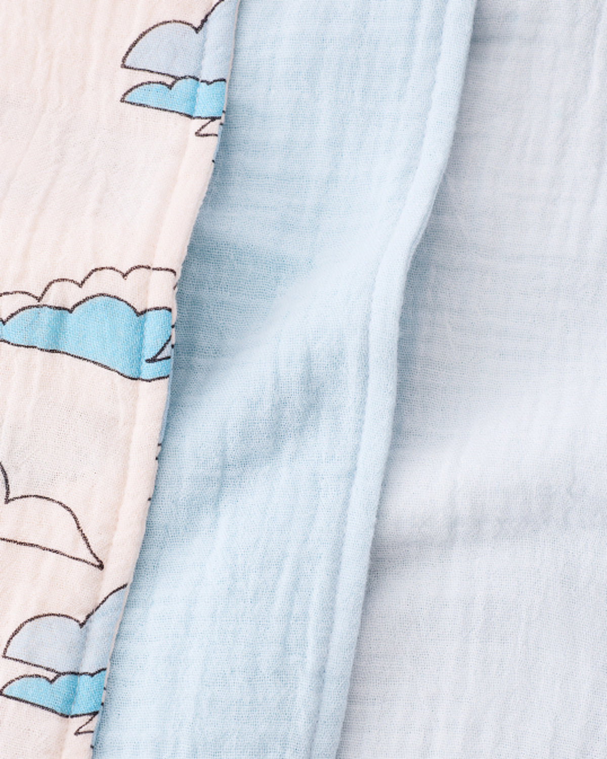 Close up of the Organic Muslin Burp Cloth (Three-Pack) in Ivory Clouds, folded and stacked, on a beige background.