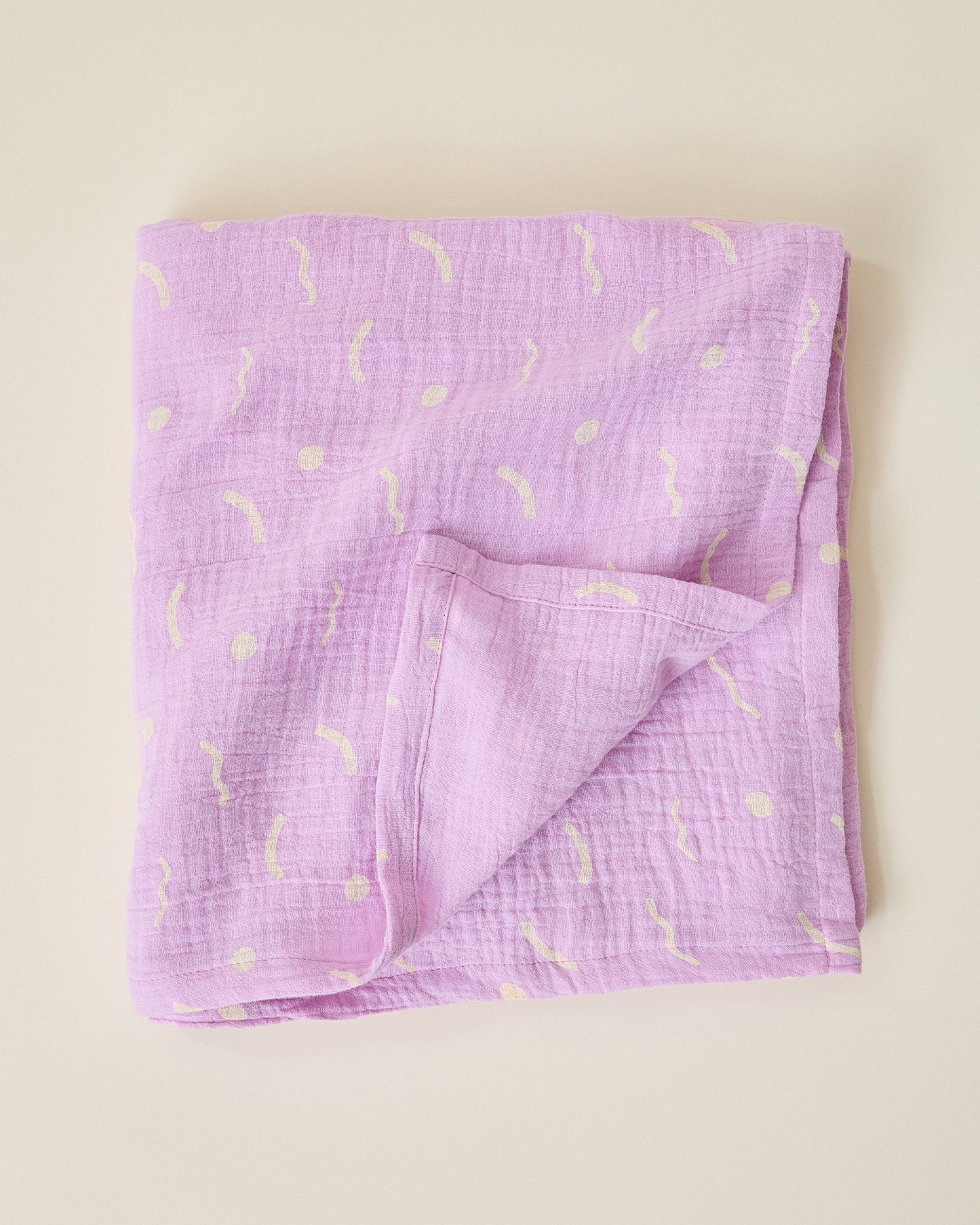 Folded purple lilac squiggles Organic Muslin Swaddle on a beige background