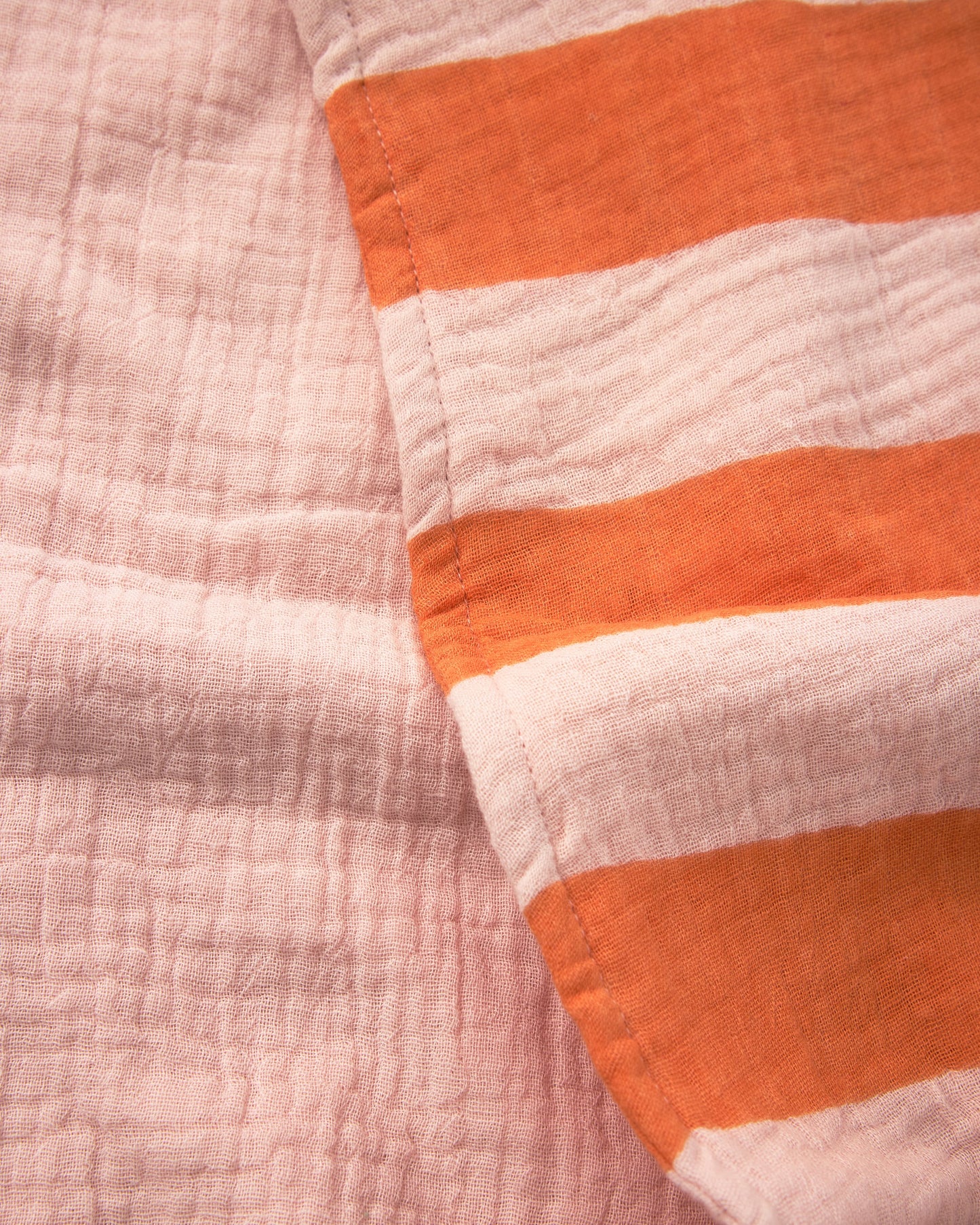 Close up of both sides of the Organic Muslin Burp Cloth (Three-Pack) in Pink Wide Stripe to show stripe side and solid pink side.
