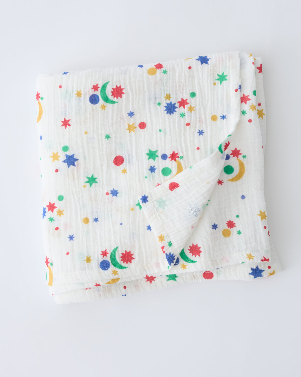 Organic Muslin Swaddle in White Starry Sky, folded with corner flipped back to show reverse side, on a beige background.