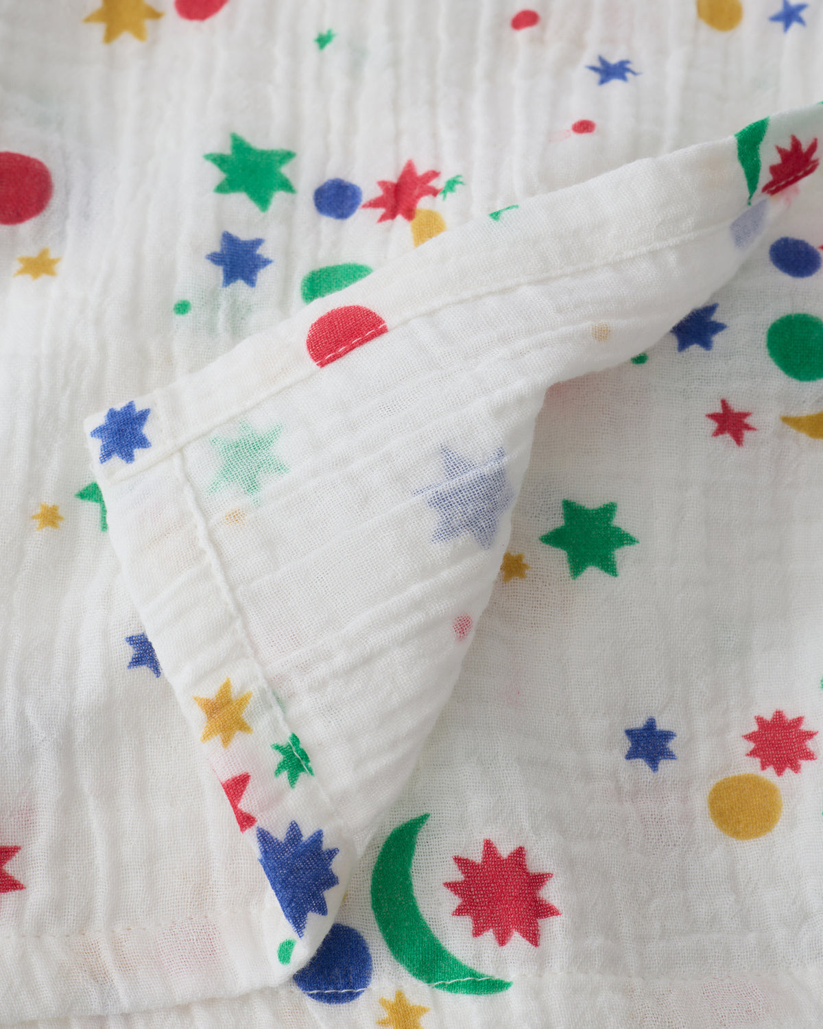 Close up of the Organic Muslin Swaddle in White Starry Sky, folded with corner flipped back to show reverse side.