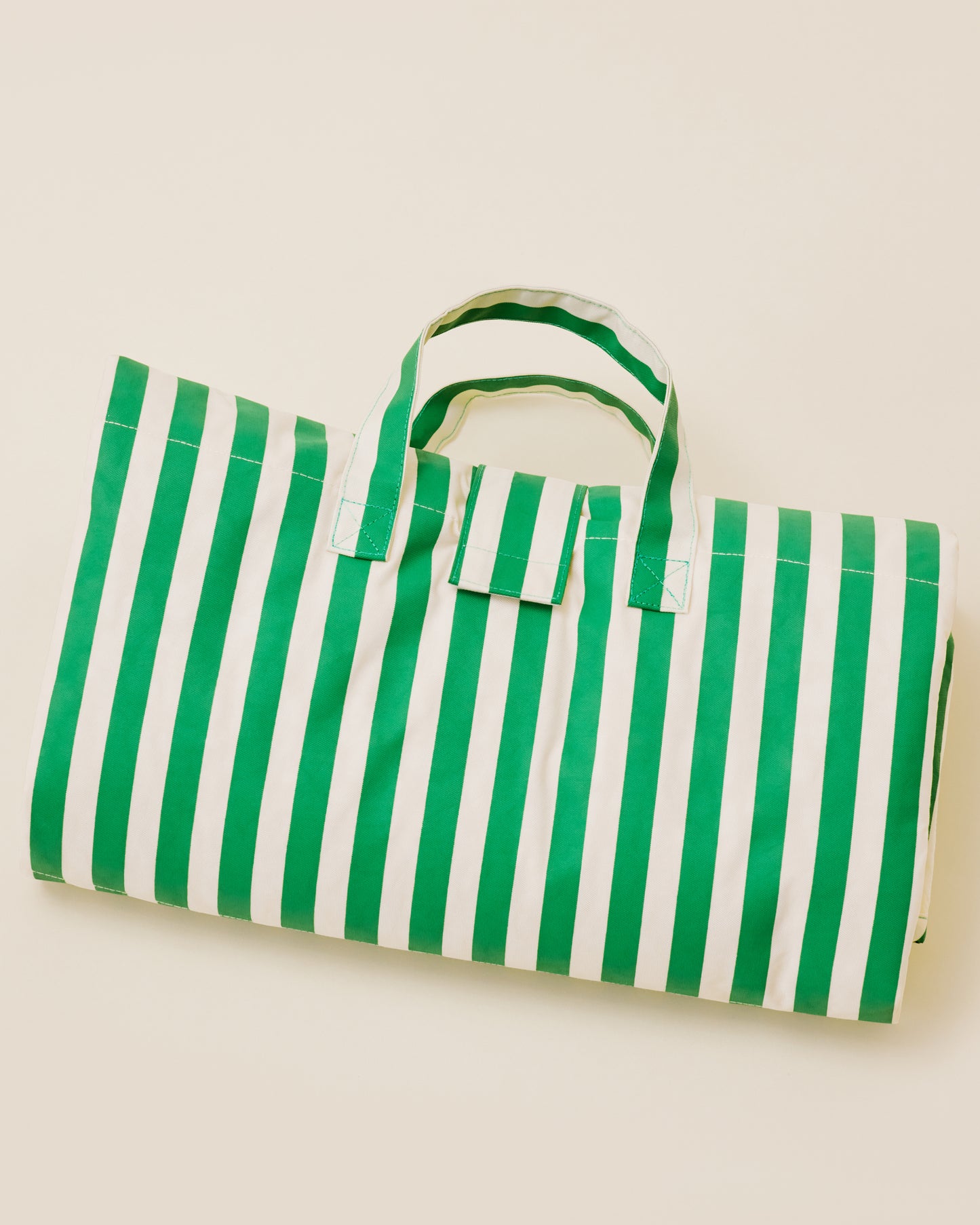 The Inside/Outside Play Mat in Green Stripes print, folded into a neat rectangle with a handle.