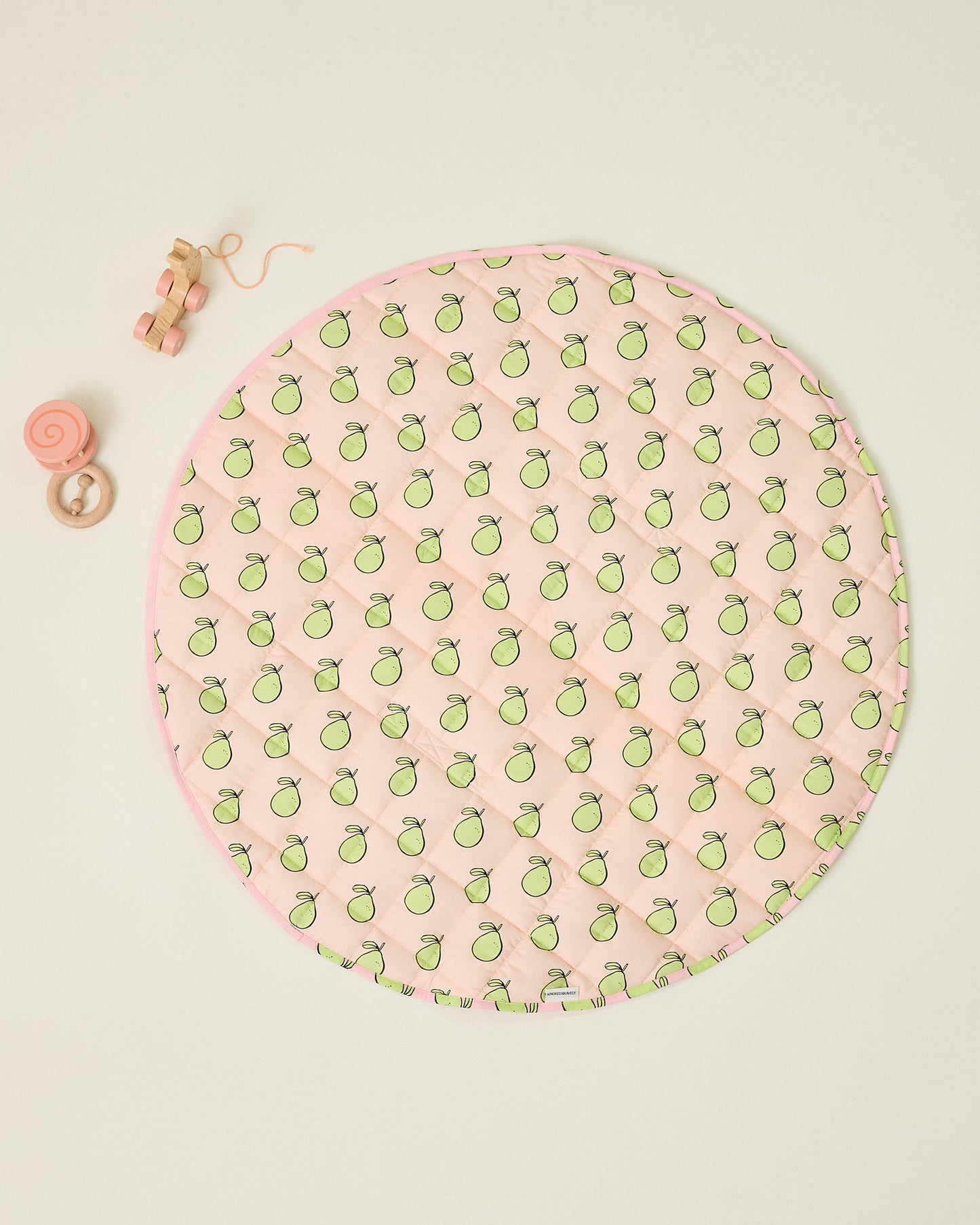 Round pink play mat with green pomelo pattern and some baby toys on a beige background