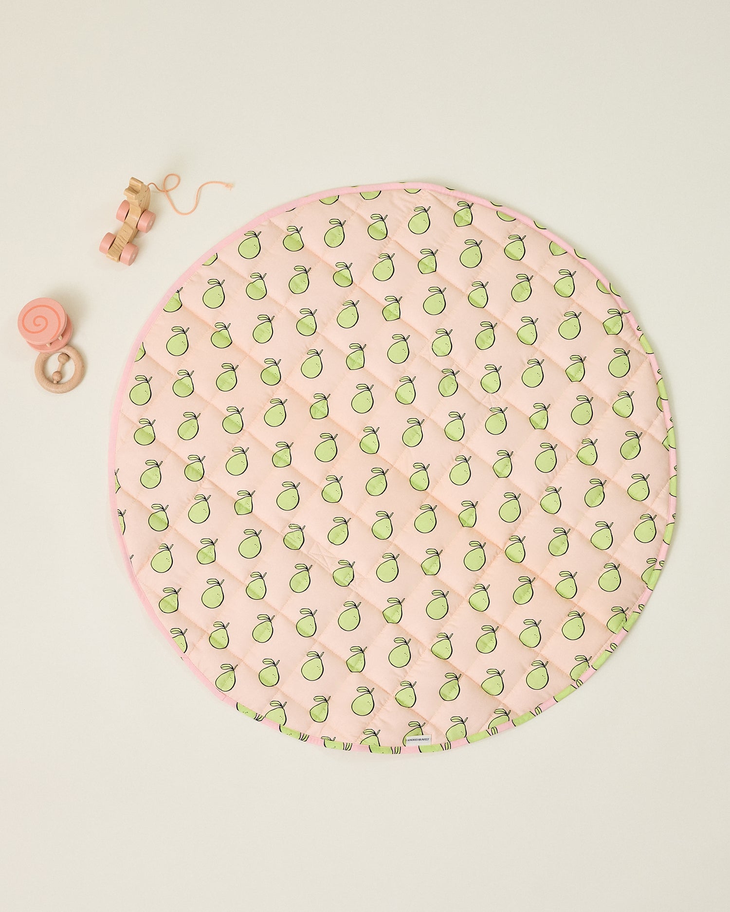 Round pink play mat with green pomelo pattern and some baby toys on a beige background