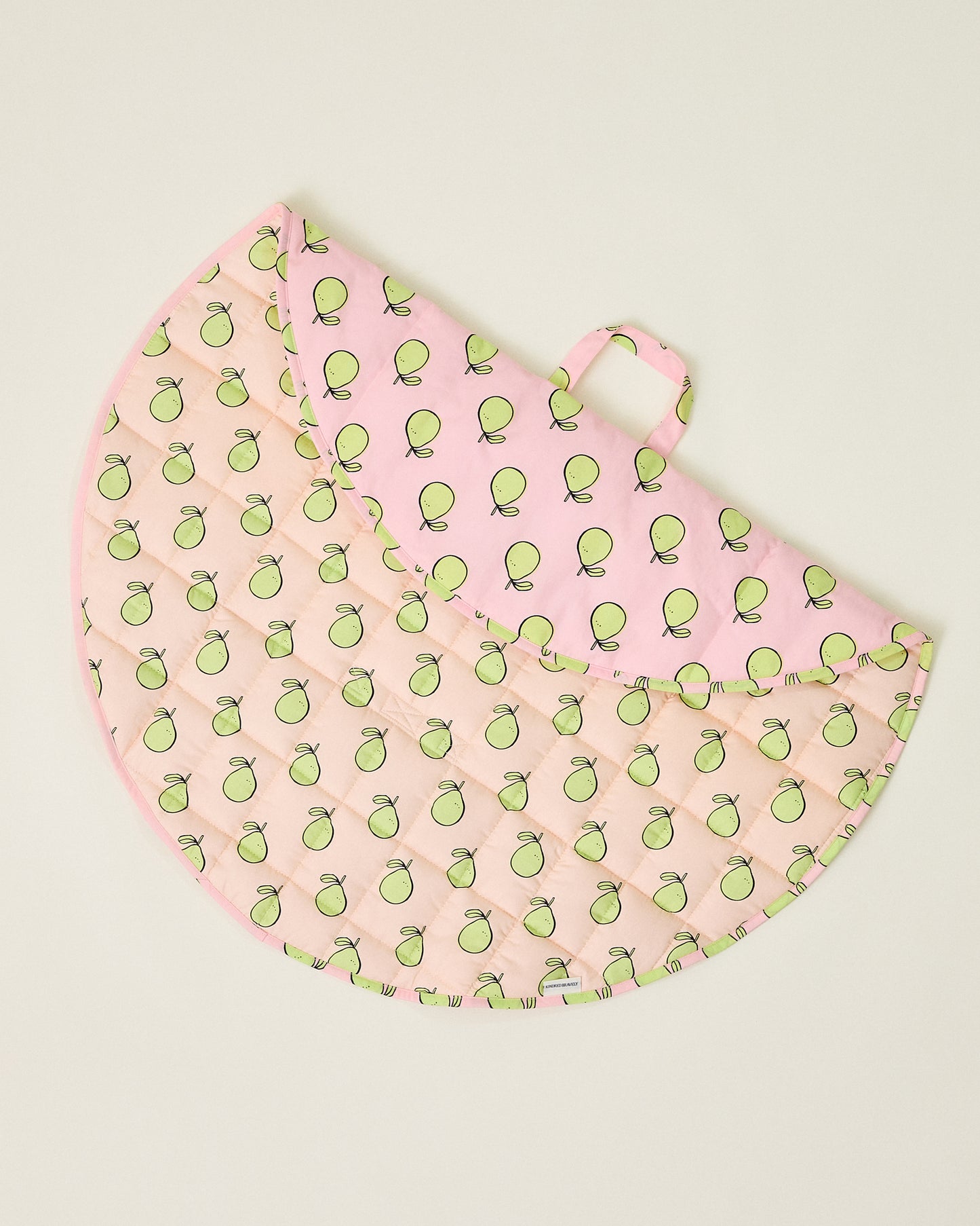 Round pink play mat with green pomelo pattern, folded over to show handle on a beige background