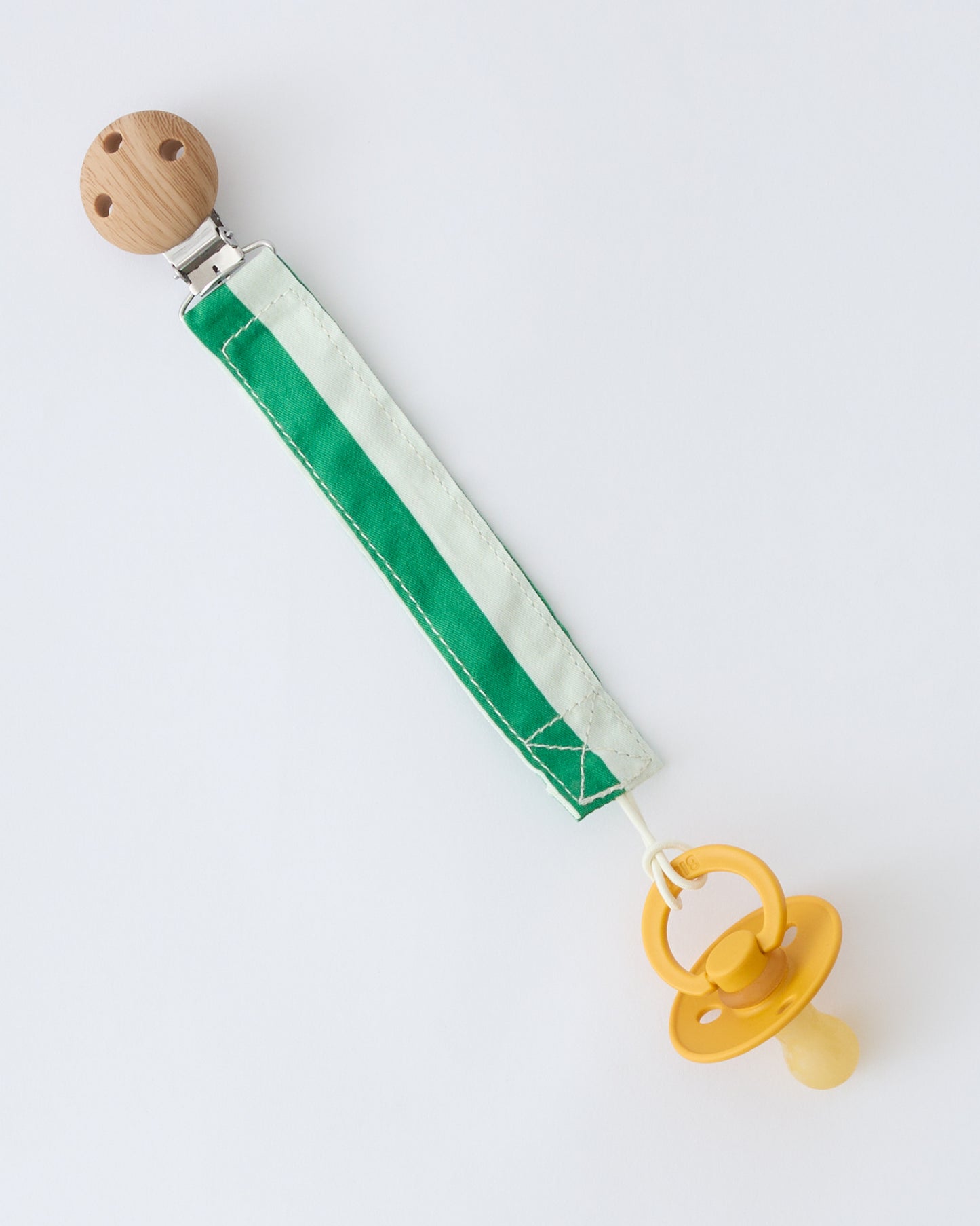 Pacifier Clip Two-Pack in Green Stripe, attached to pacifier, on a beige background.