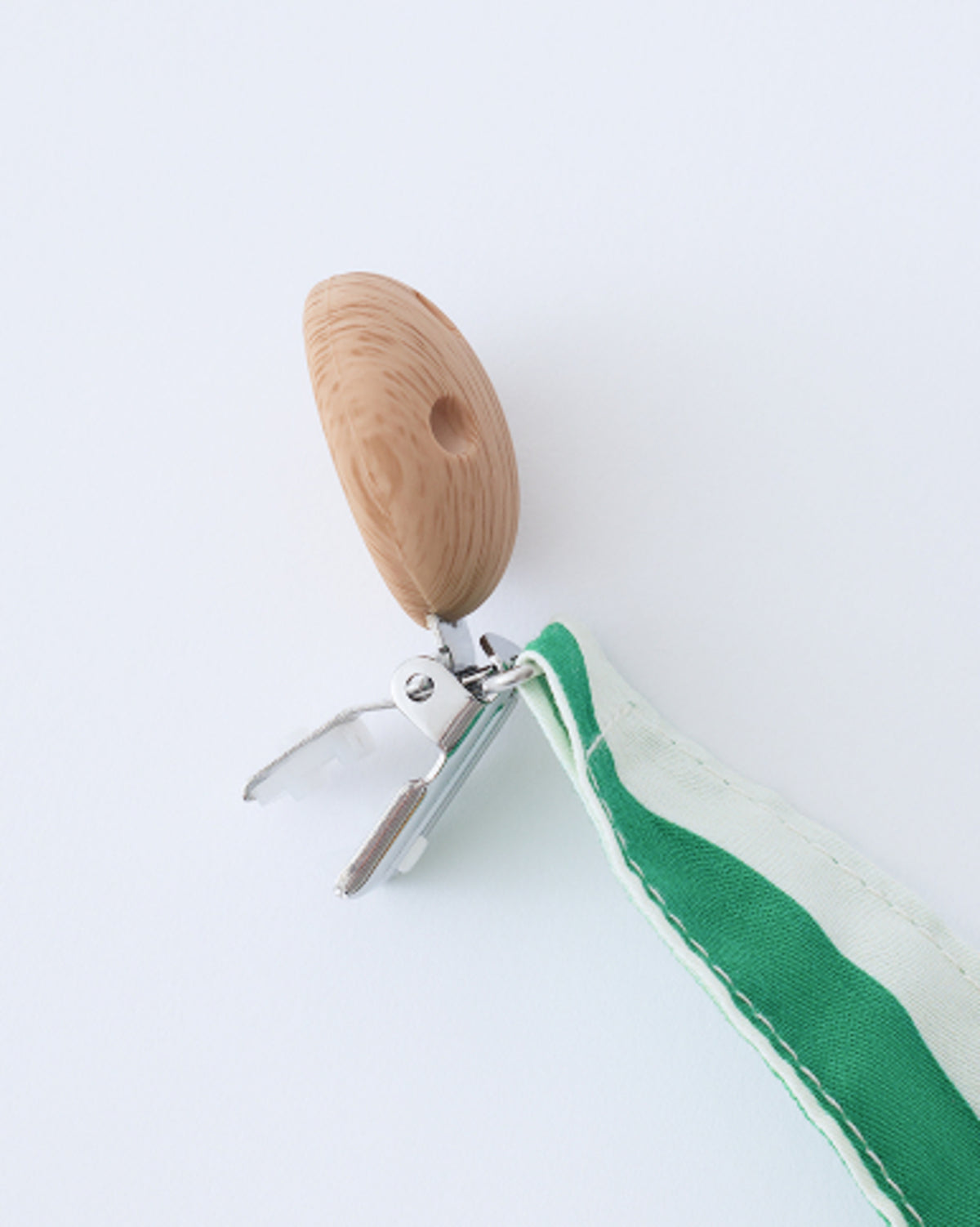 Close up of the clip of Pacifier Clip Two-Pack in Green Stripe, on a beige background.