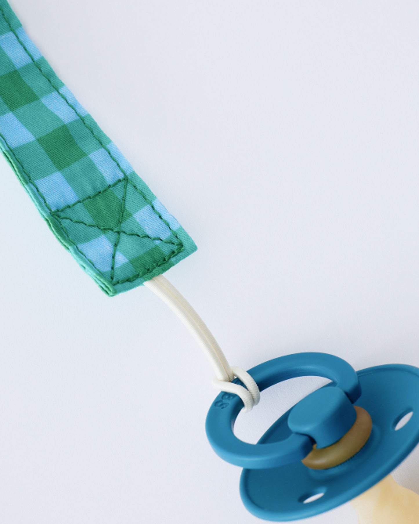 Close up of elastic cord on the Pacifier Clip Two-Pack in Teal Gingham on a beige background.
