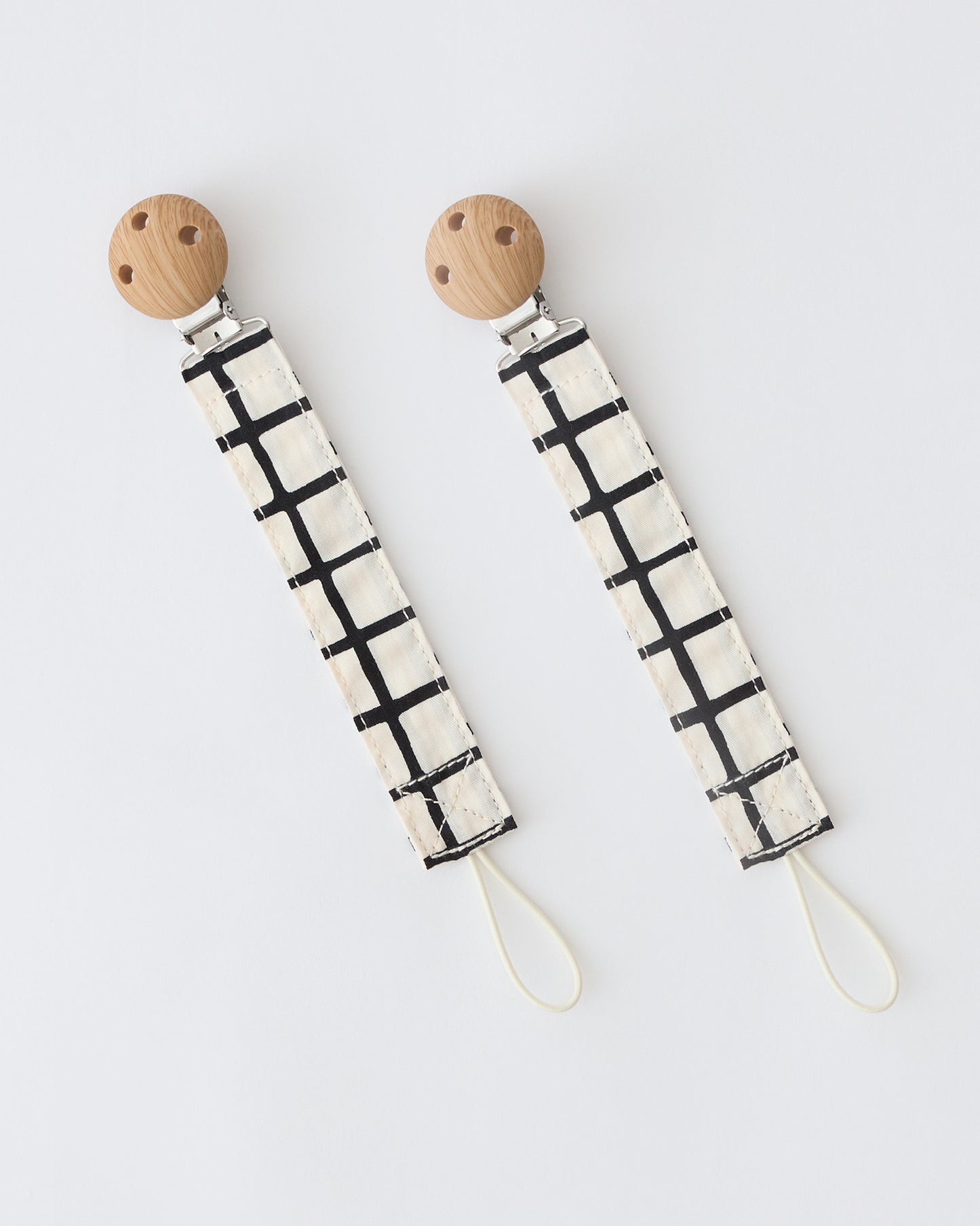 Pacifier Clip Two-Pack in Black Grid,  on a beige background.