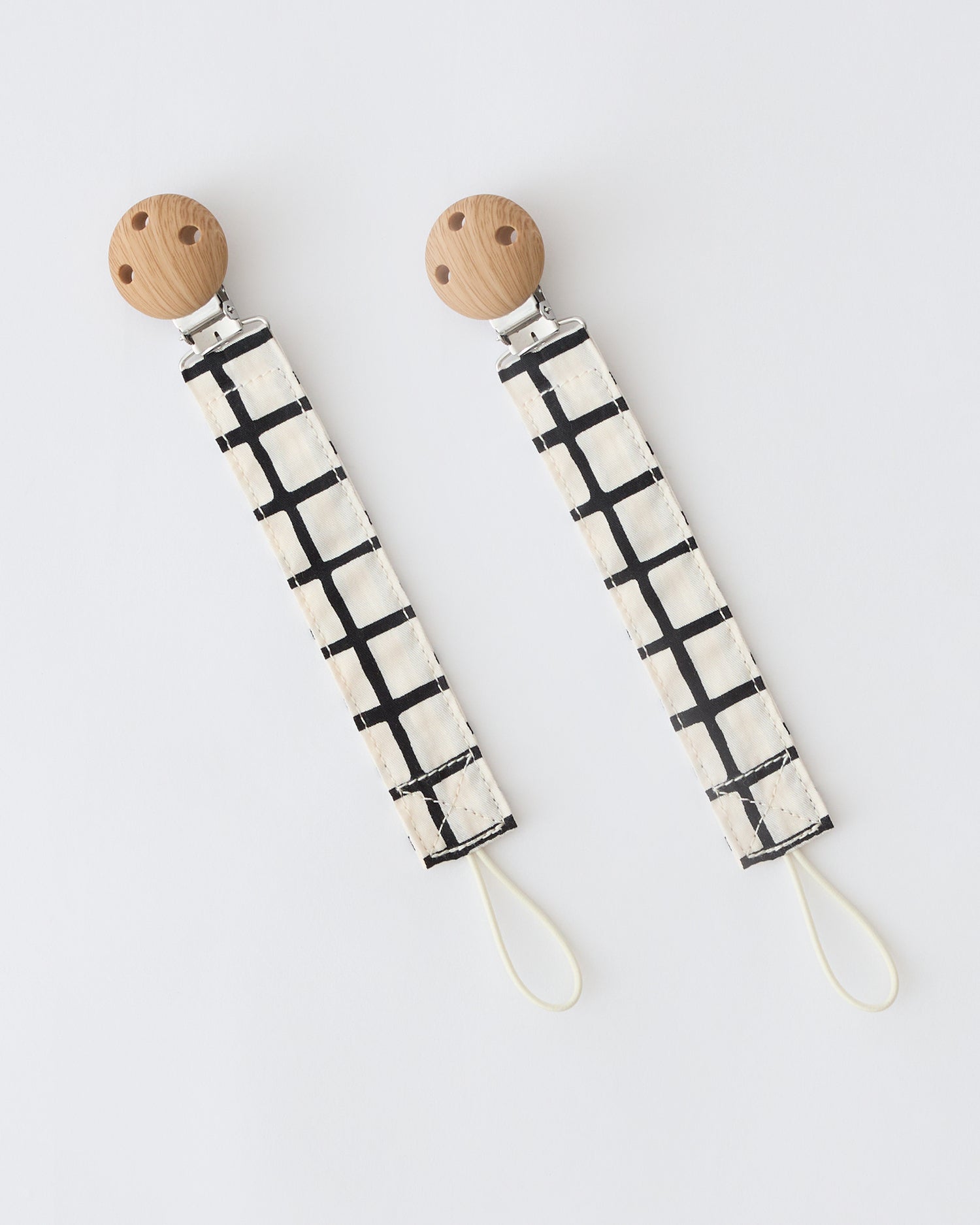Pacifier Clip Two-Pack in Black Grid,  on a beige background.